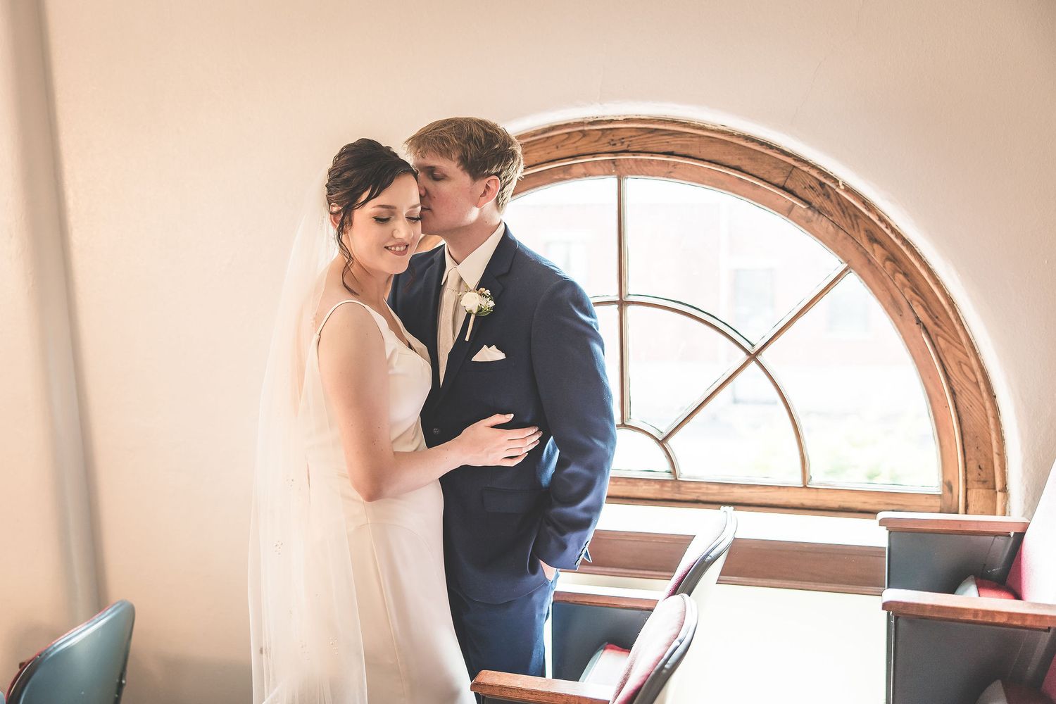 Intimate wedding moment captured in a sunlit theater with arched windows and warm tones.