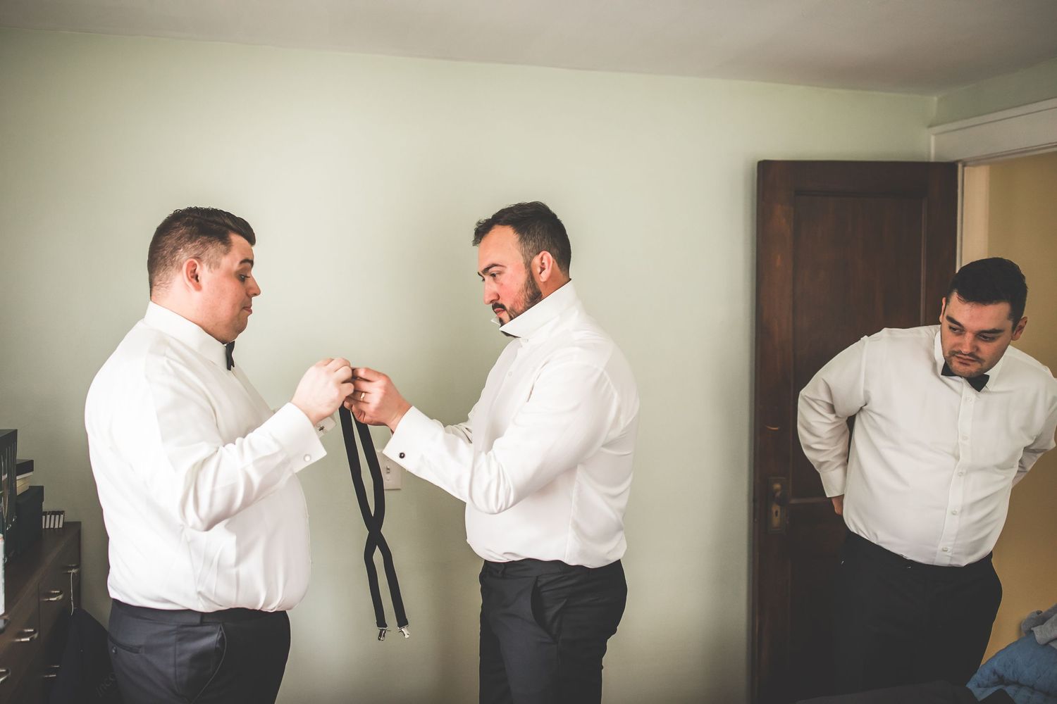 Two people in white dress shirts helping each other with formal neckwear preparations.