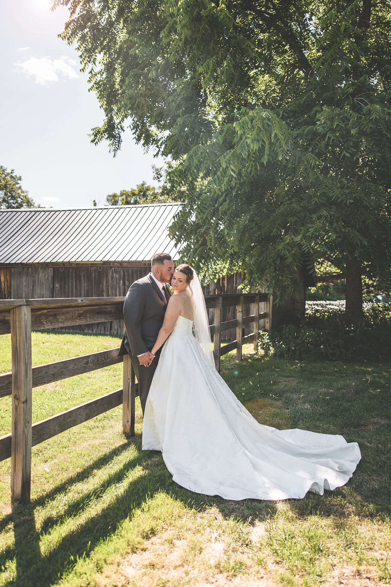 Wedding portraits by a wooden fence with a flowing white dress catching the sunlight.