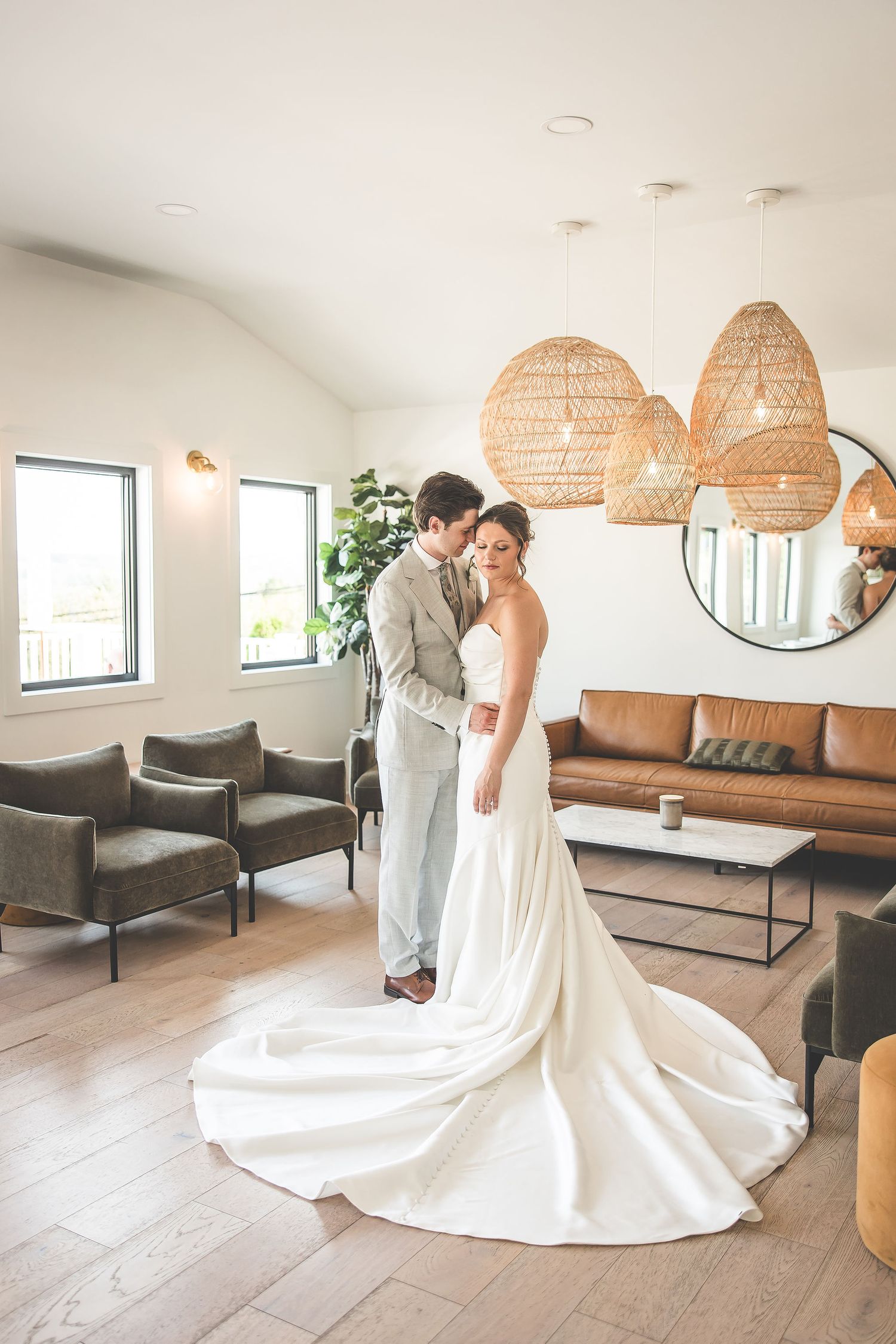 Elegant white wedding dress with a flowing train photographed in a modern room with woven pendant lights.