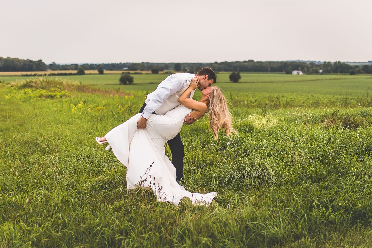 Romantic couple poses in a lush green field during golden hour wedding photography session.