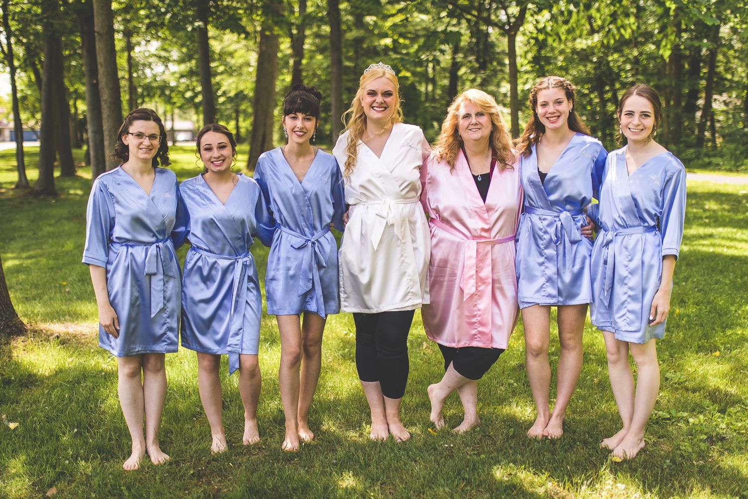 Bridesmaids in light blue dresses stand together outdoors in a garden setting.