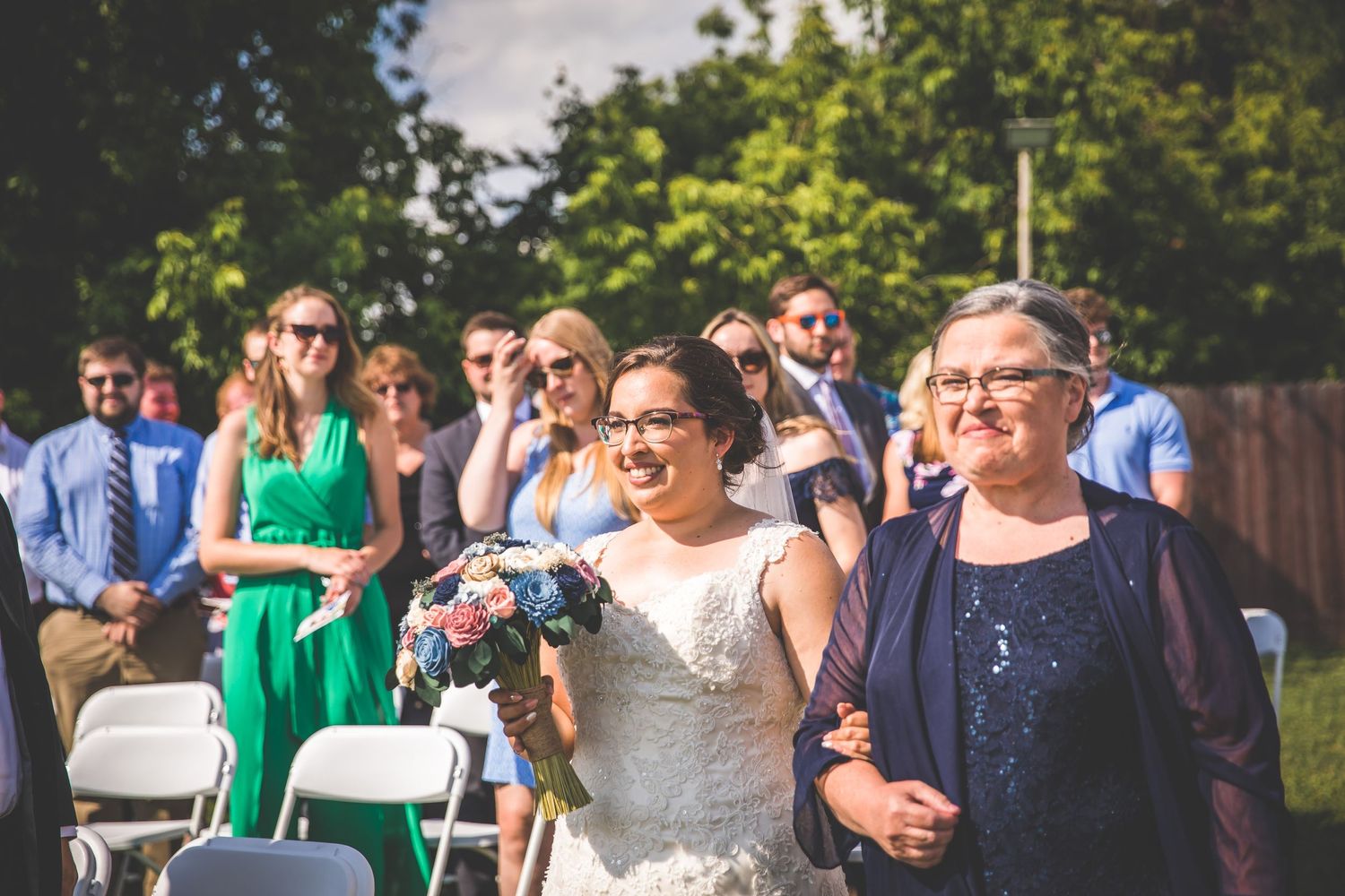 Wedding guests gather outdoors during a sunny daytime celebration.