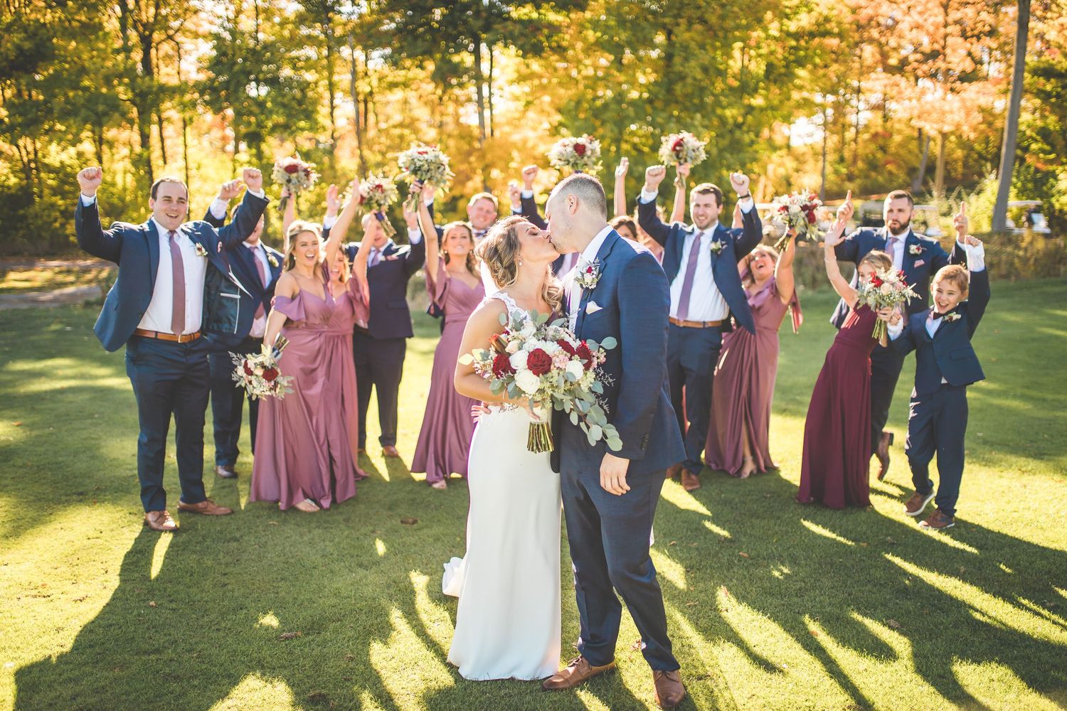 Wedding party and guests gather on a lawn during golden hour.