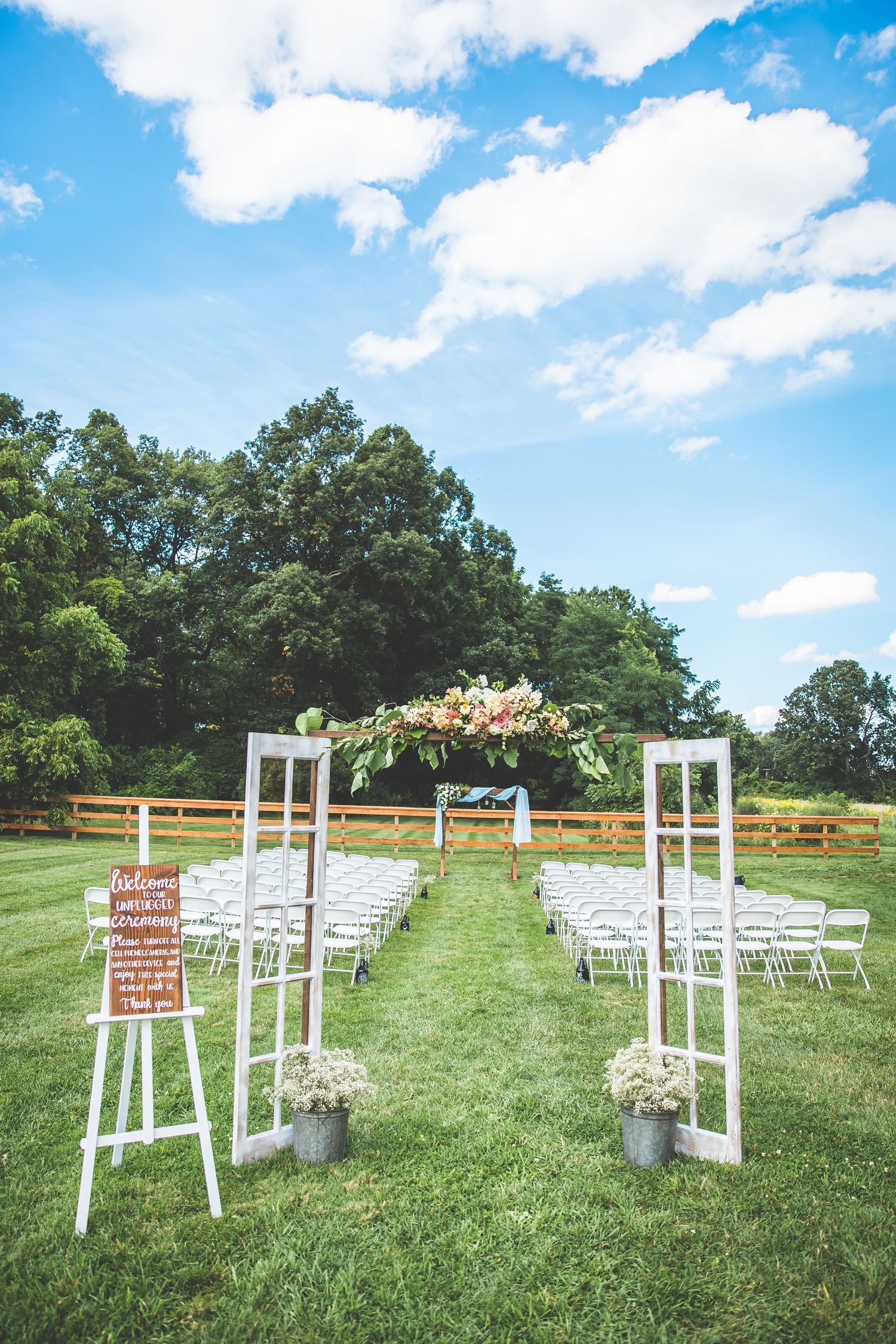 Outdoor wedding ceremony setup with white chairs and wooden posts on a rolling green lawn.