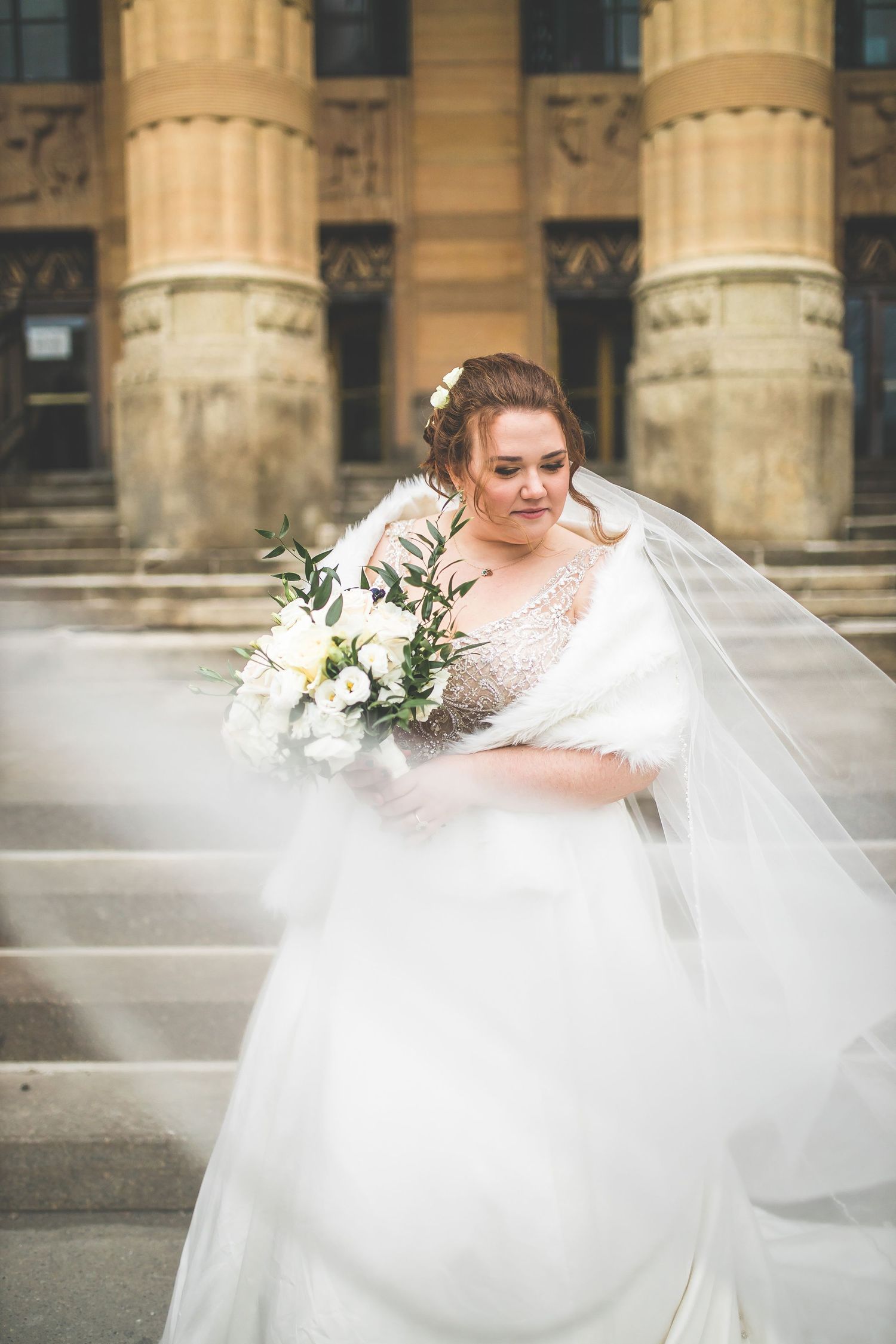 Bride in flowing white gown with bouquet posing on stone steps.