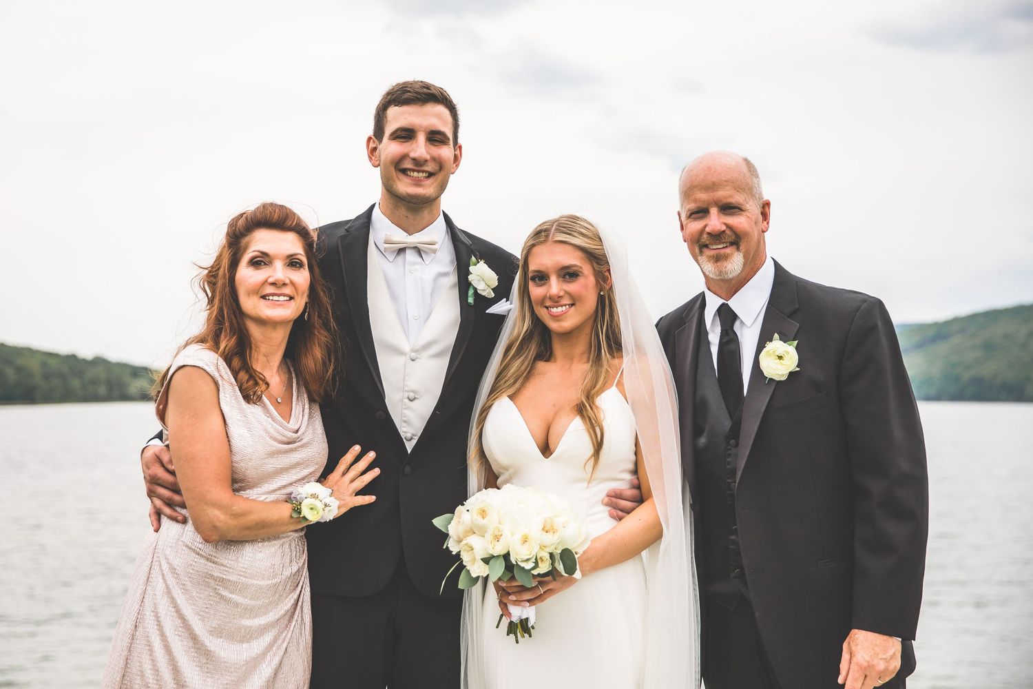 Wedding party group photo with scenic lake backdrop.