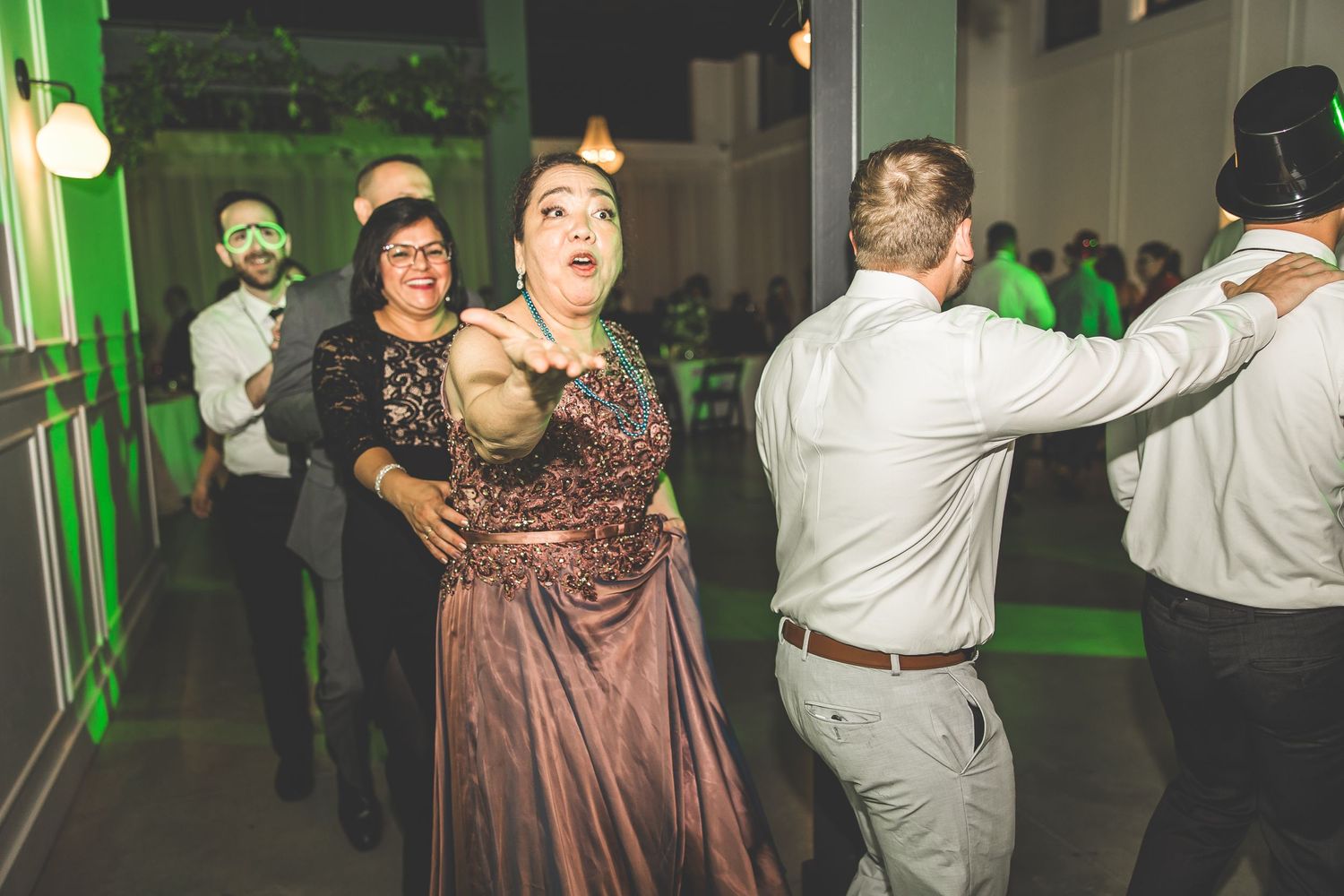 Wedding guests dancing energetically at reception with green lighting effects.