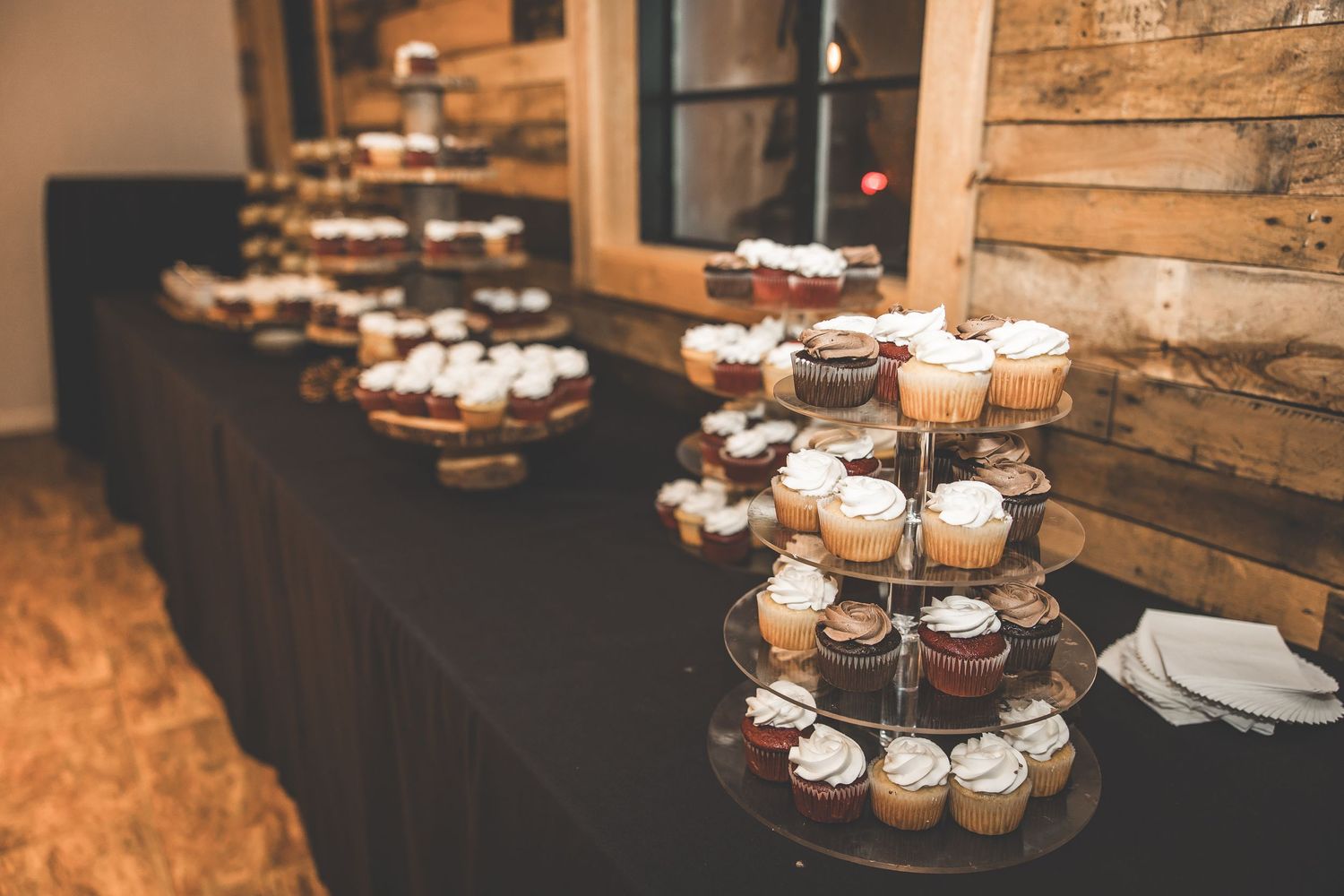 Rustic wedding dessert table display with cupcakes and treats on wooden surfaces.