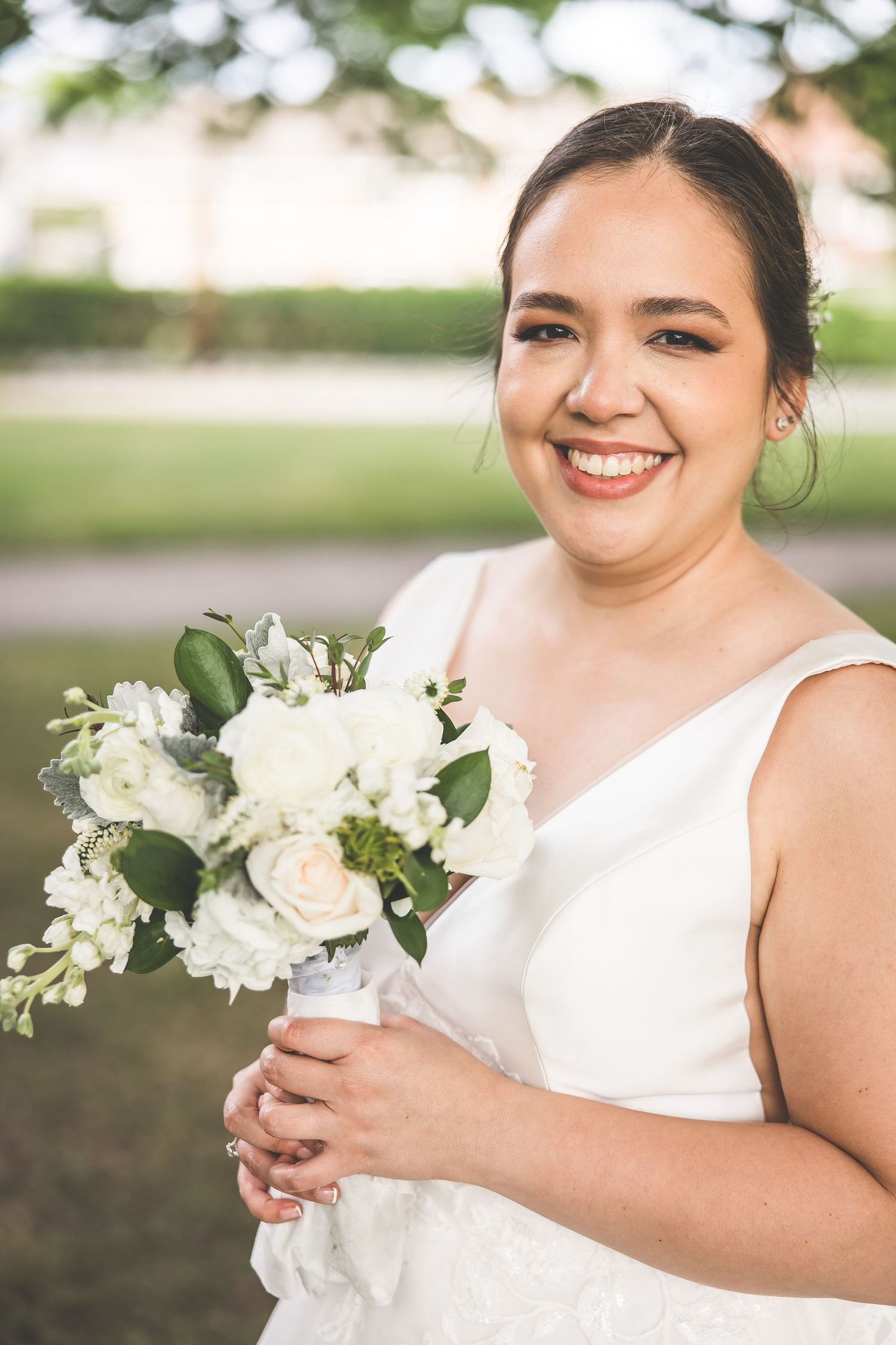 White floral bouquet complements elegant sleeveless wedding gown in natural light.
