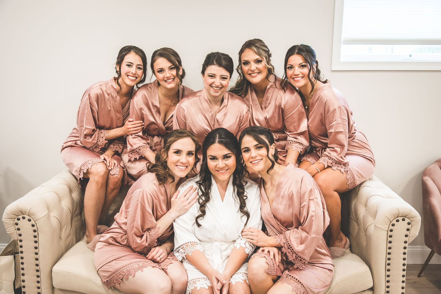 Bridesmaids in pink silk robes pose together during pre-wedding festivities.