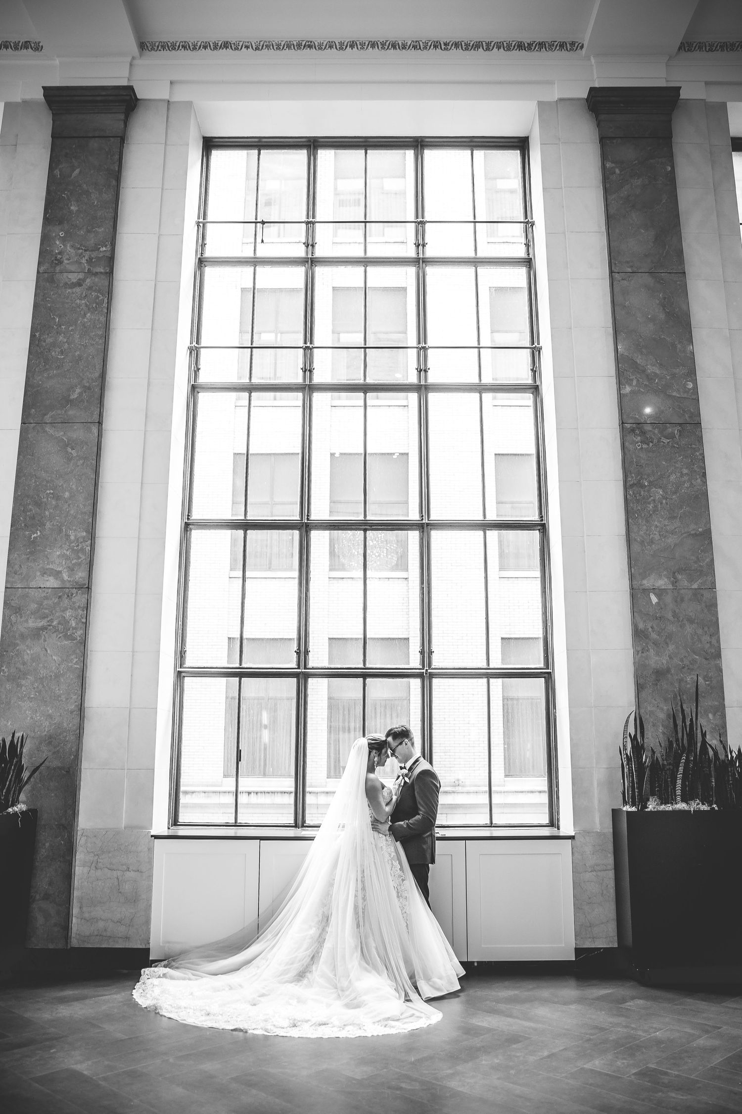 A dramatic black and white wedding portrait in front of a tall architectural window.
