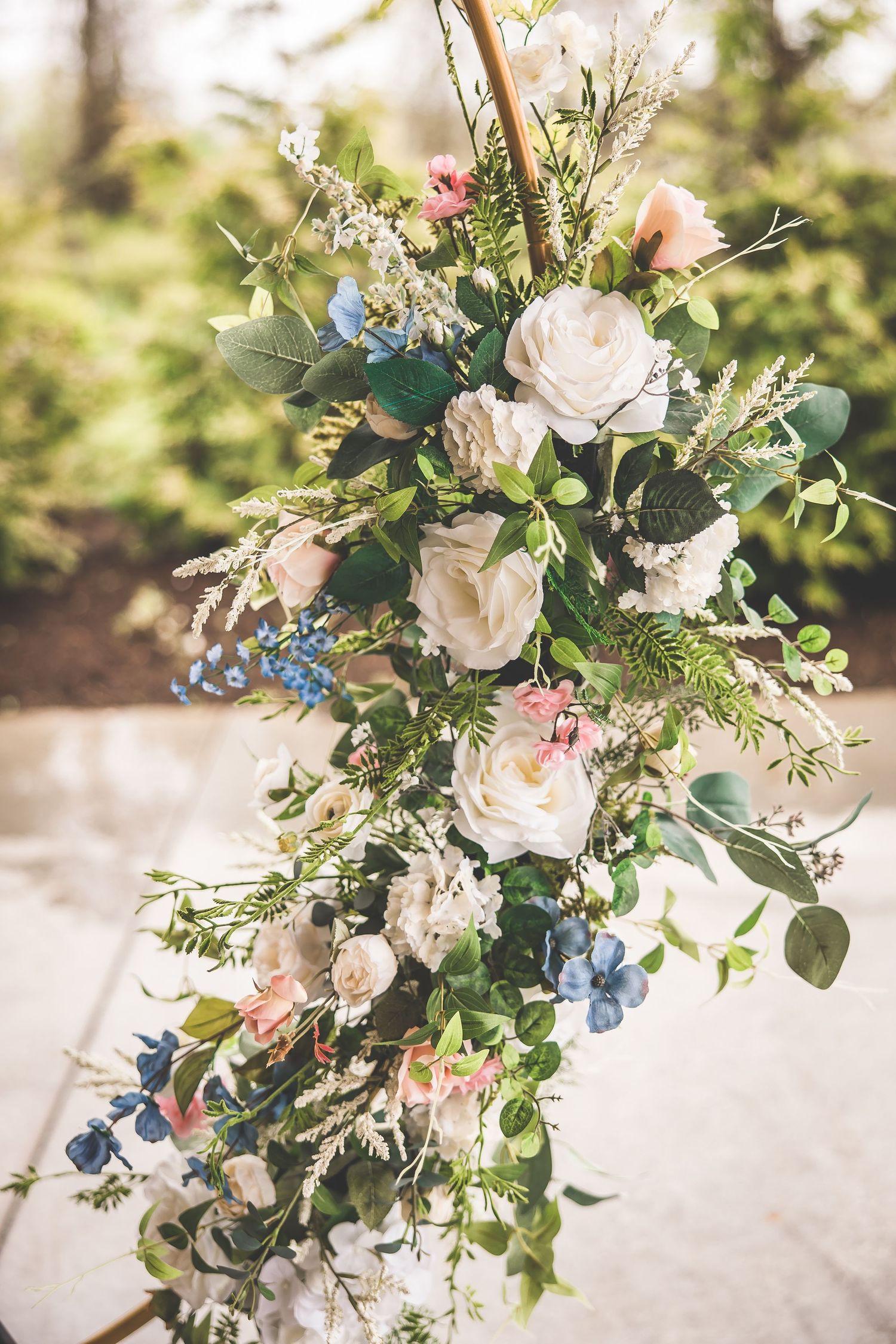 A romantic floral arrangement featuring white roses, blue flowers, and greenery in natural sunlight.