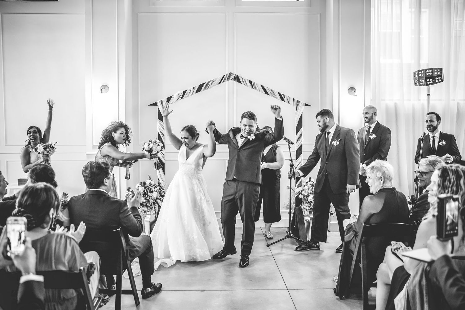 Wedding guests gather in a bright reception hall with white walls and modern decor.