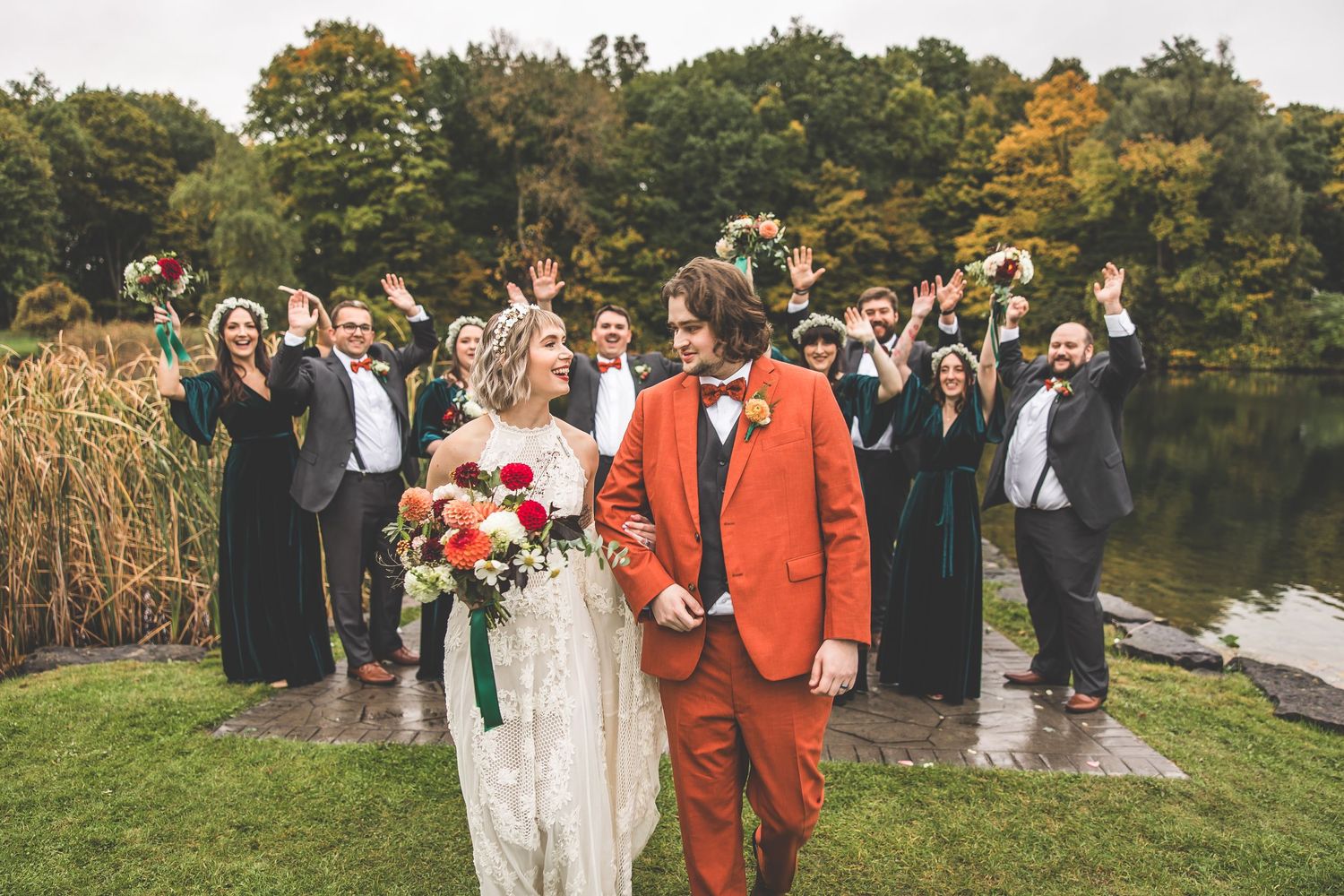 A wedding party stands on a grassy lawn with autumn trees in the background during an outdoor ceremony.