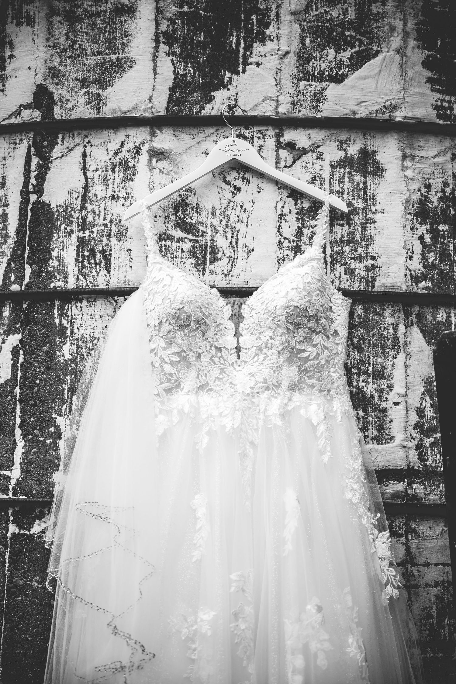 Black and white image of an elegant white wedding dress with lace details displayed outdoors.