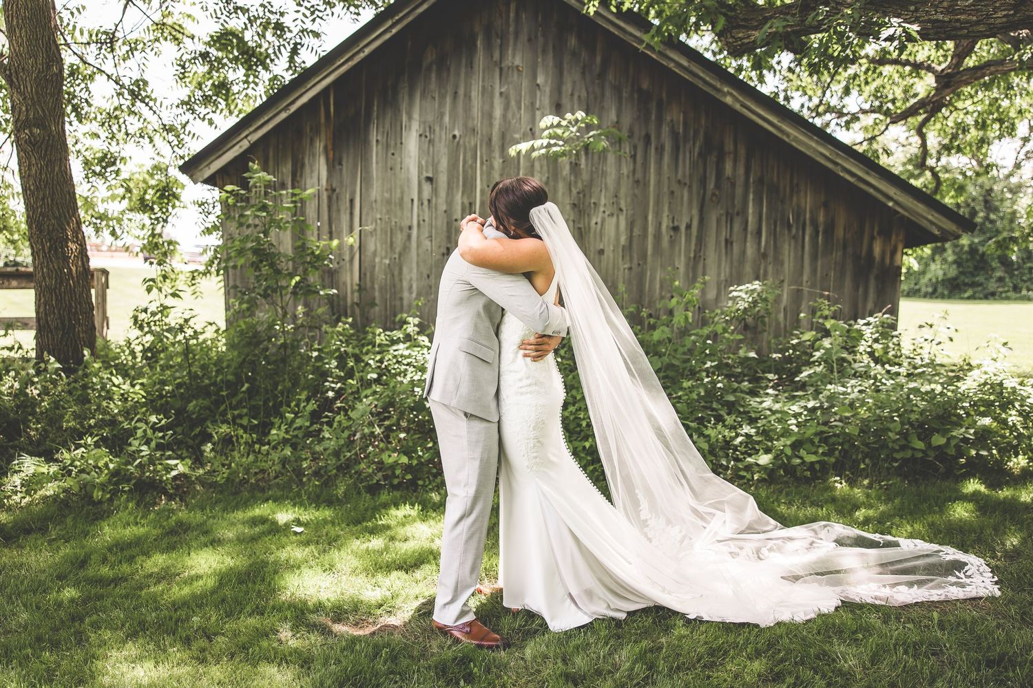 Wedding couple shares intimate moment by rustic barn with flowing white dress.