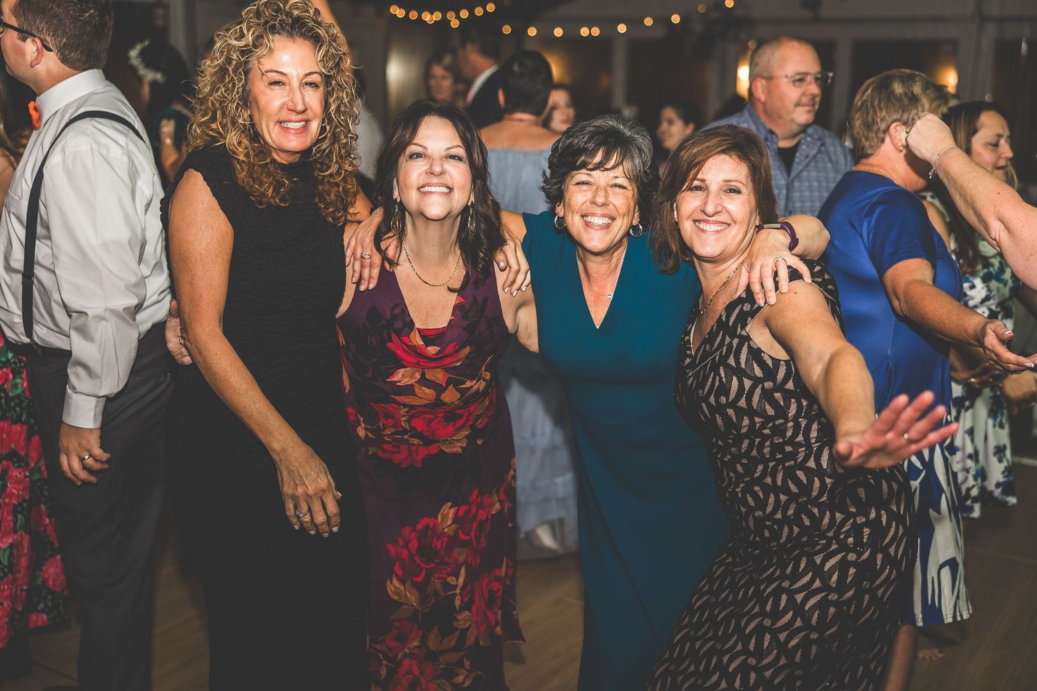 Group of wedding guests dancing together in formal attire at an indoor reception.