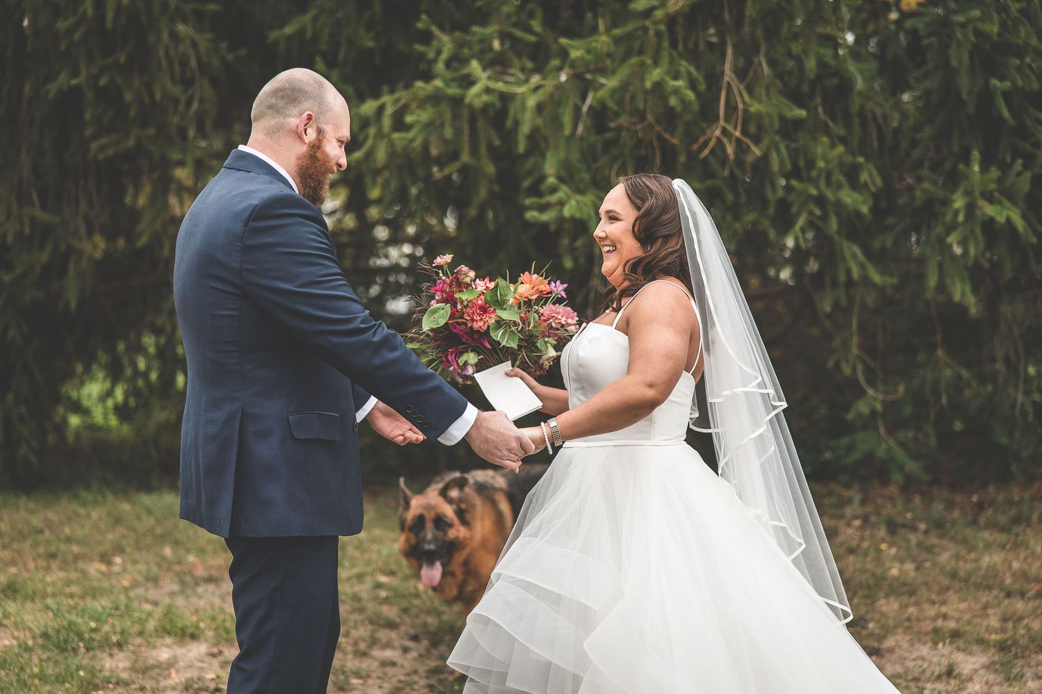 A couple in wedding attire shares an emotional moment during their first look in a natural outdoor setting.
