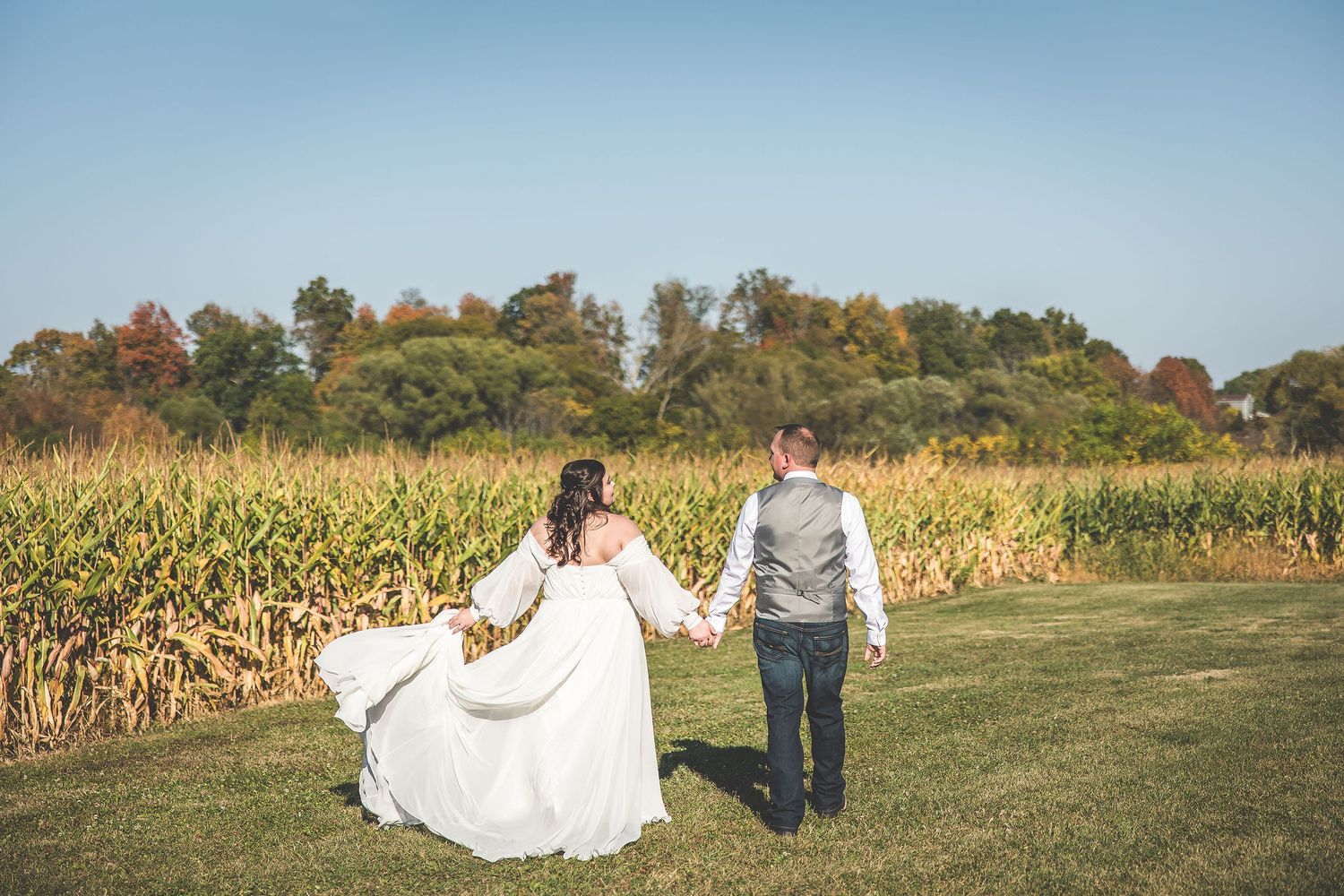 Wedding photography session in a cornfield with distant barn and autumn landscape.
