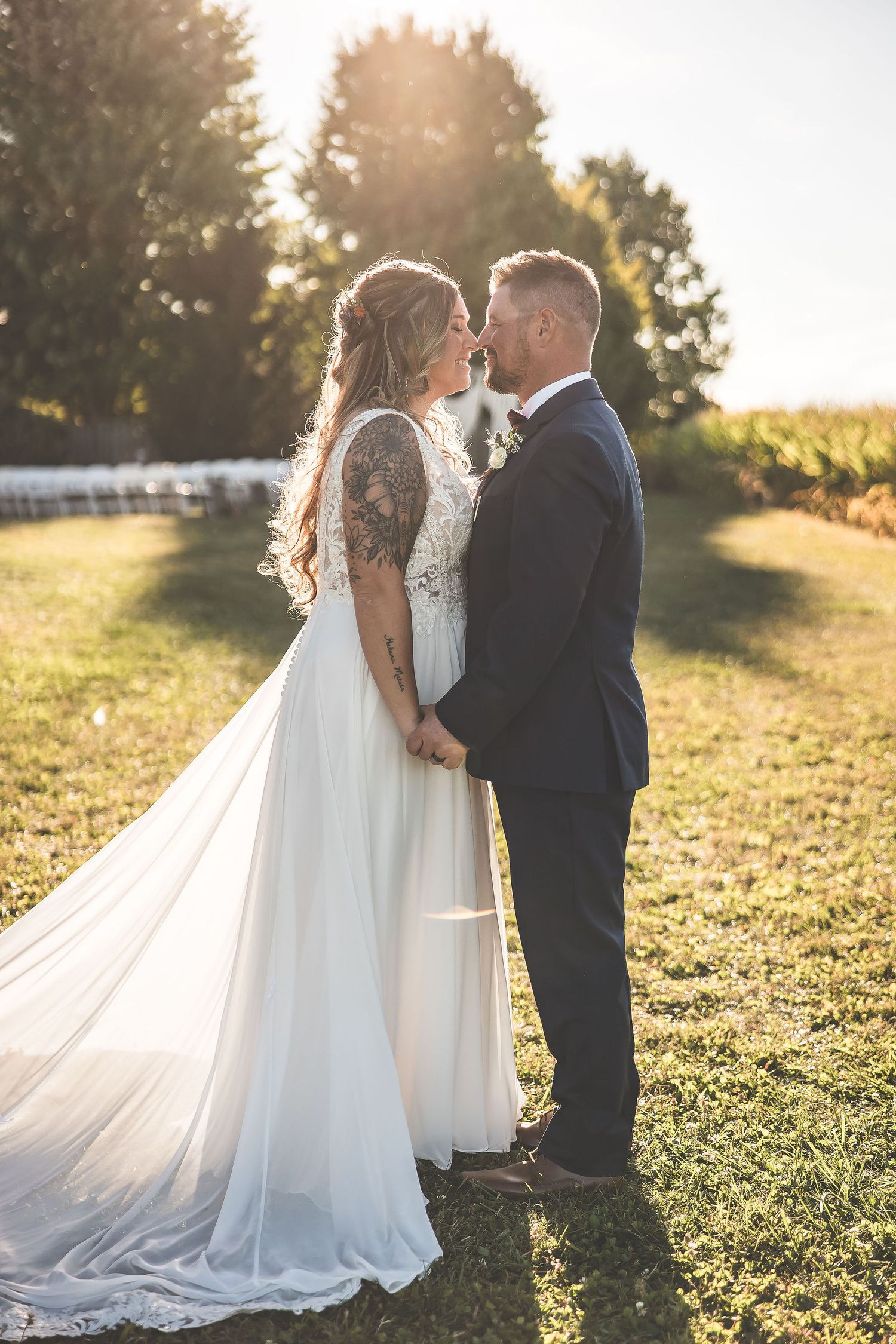 Sunset wedding portrait with flowing white dress train in golden field.