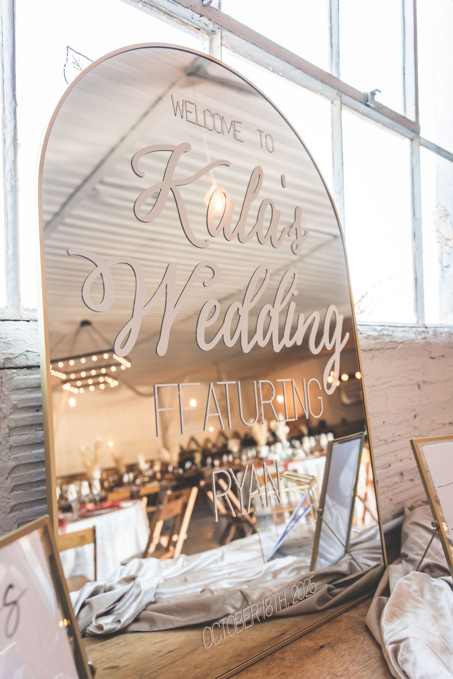 Decorative mirror signage welcoming guests to an event with string lights reflected.