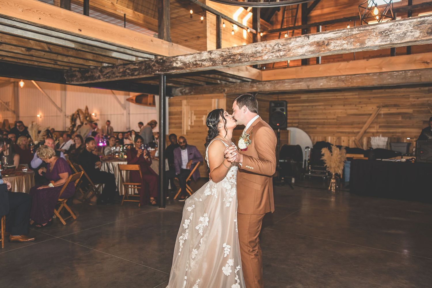 A couple dances in an industrial-style venue with exposed wooden beams and ambient lighting.