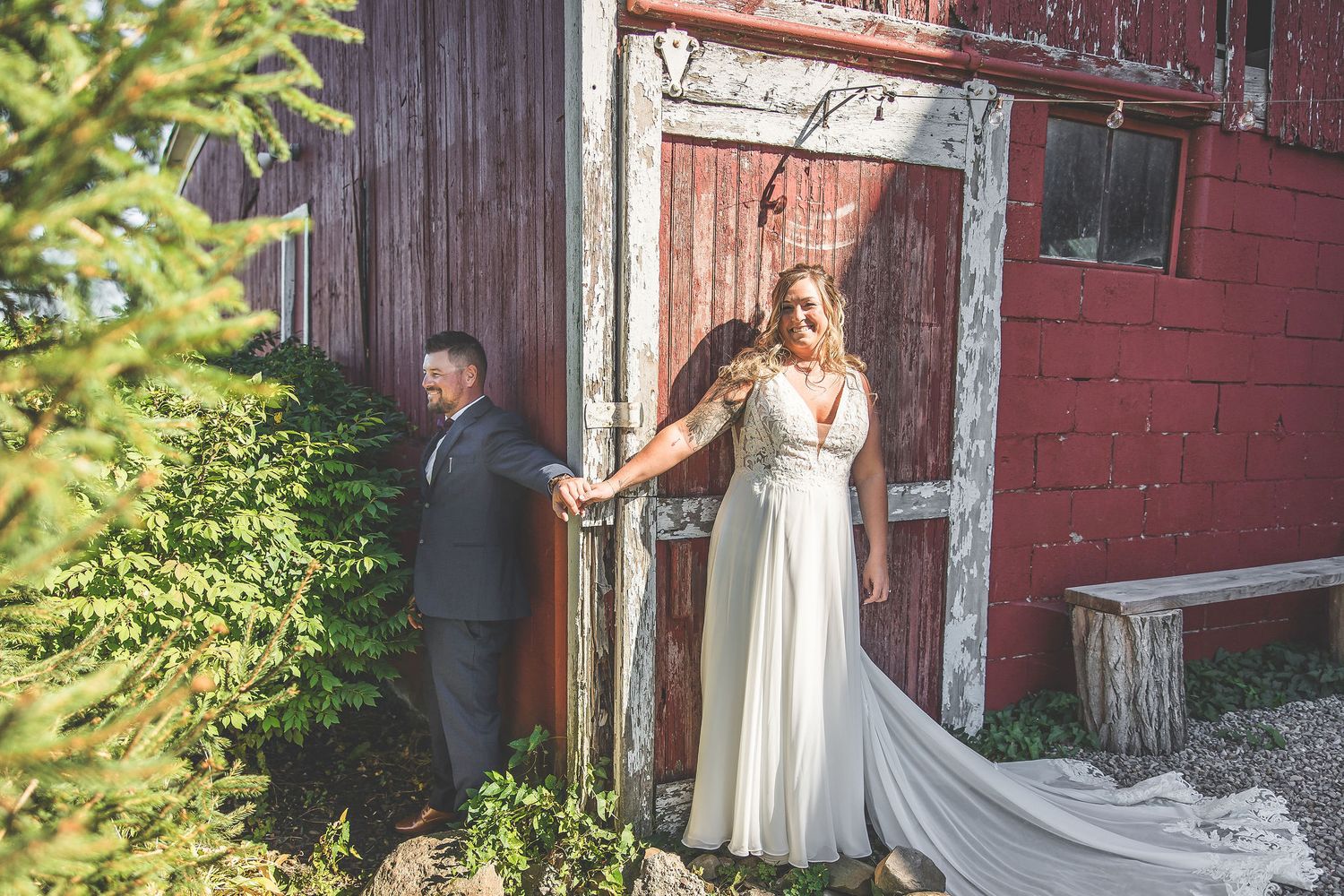 Rustic barn wedding photos featuring couple against faded red wooden walls.