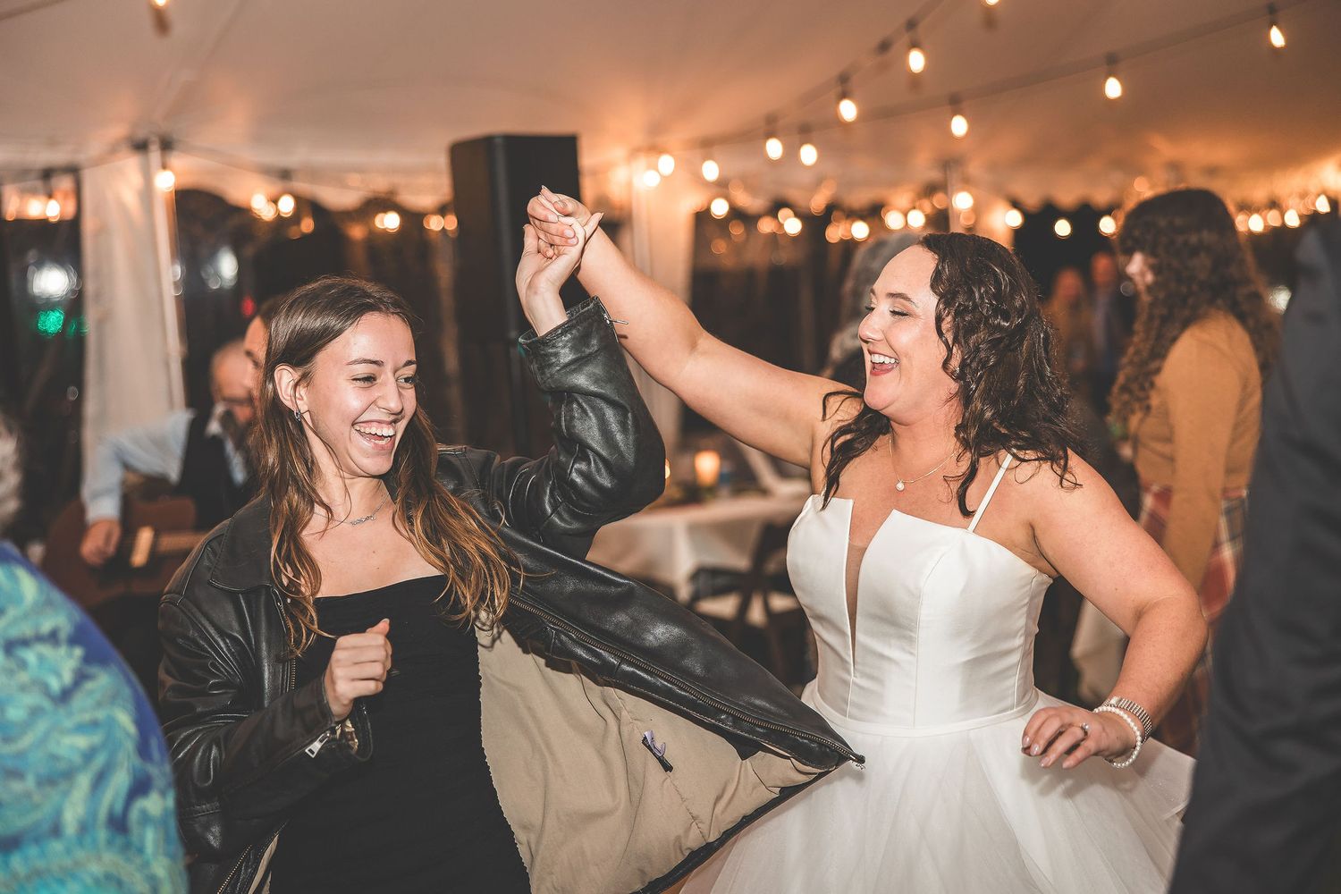 Wedding guests dancing and laughing together under warm string lights at an evening celebration.