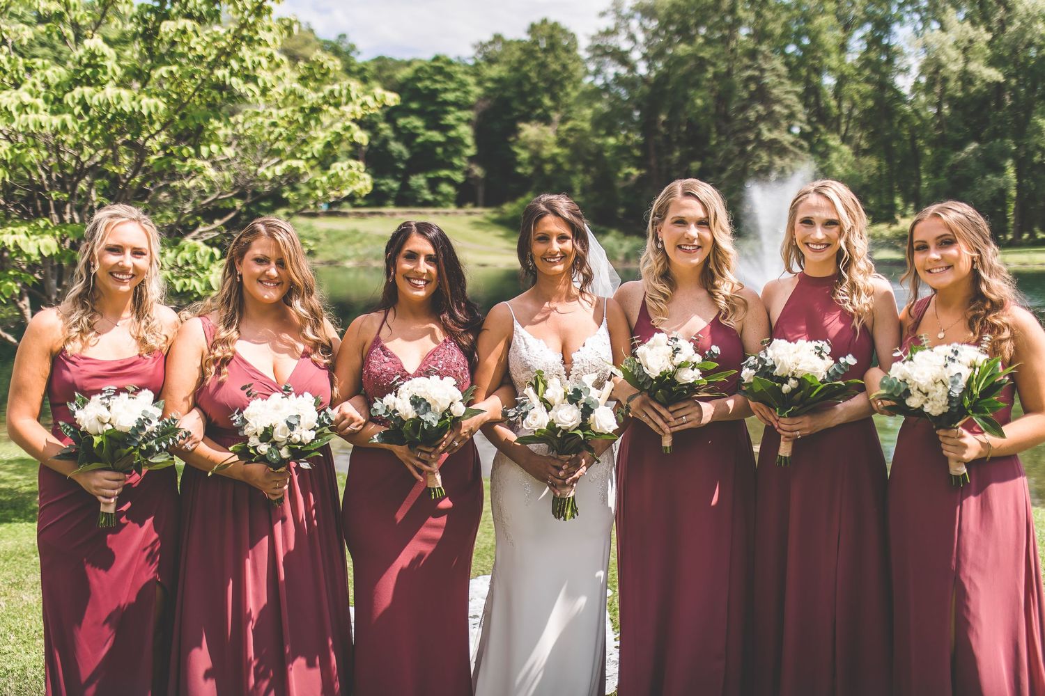 Wedding party lined up outdoors with burgundy dresses against a natural landscape setting.