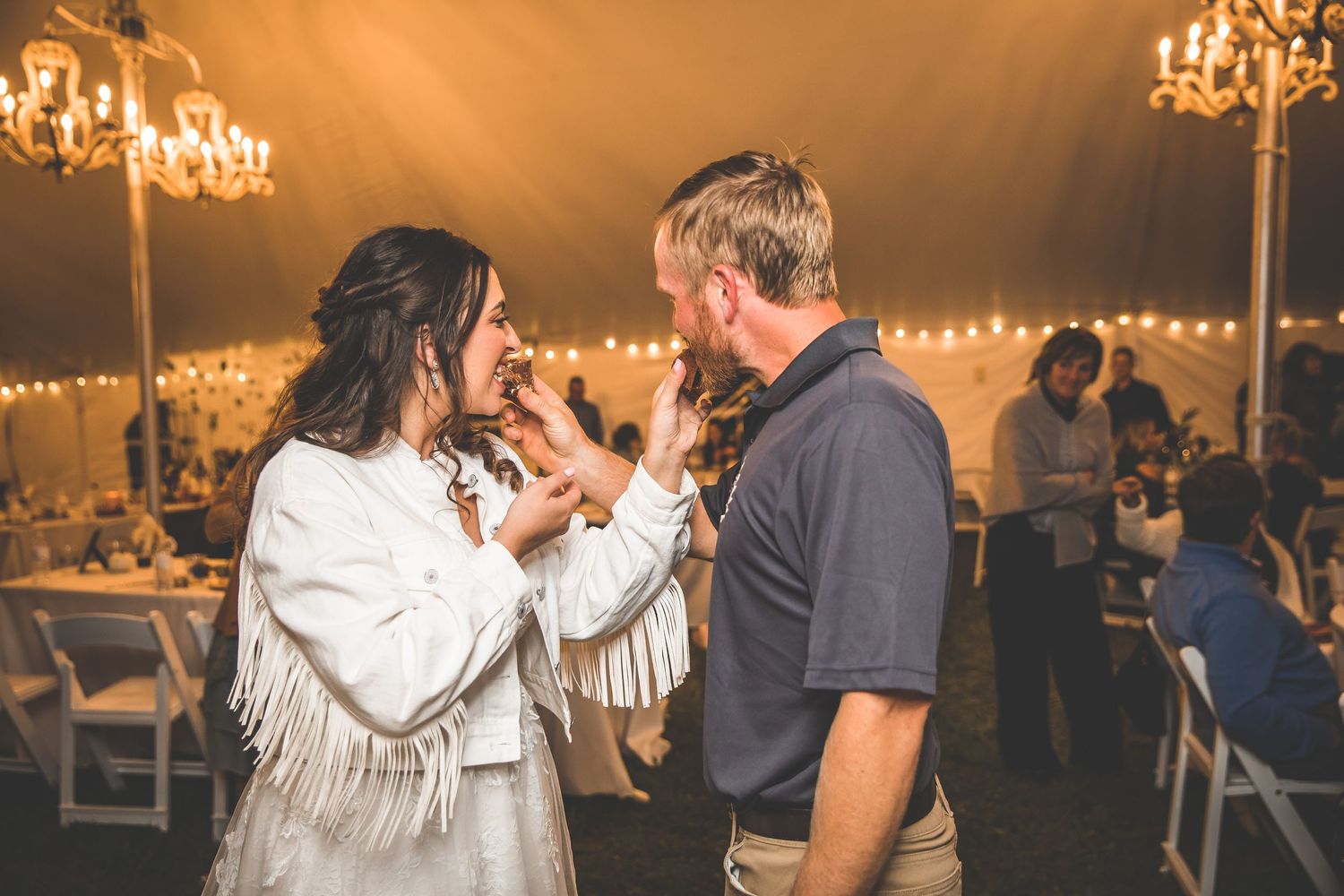 Wedding reception tent illuminated by warm lighting and crystal chandeliers.
