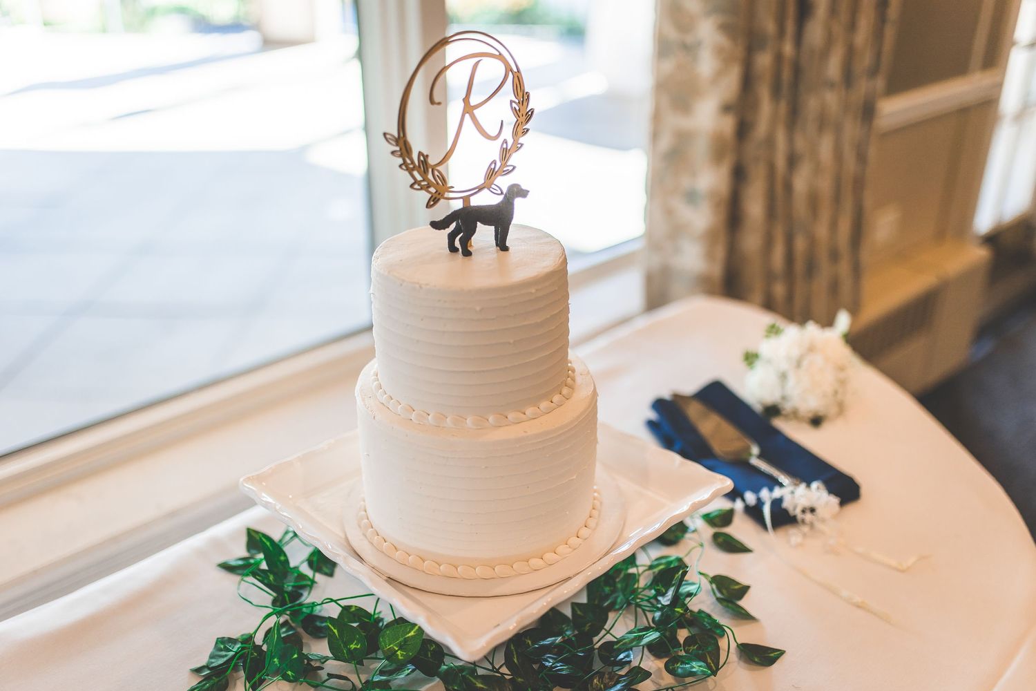 Elegant white wedding cake with simple textured design on display near window.