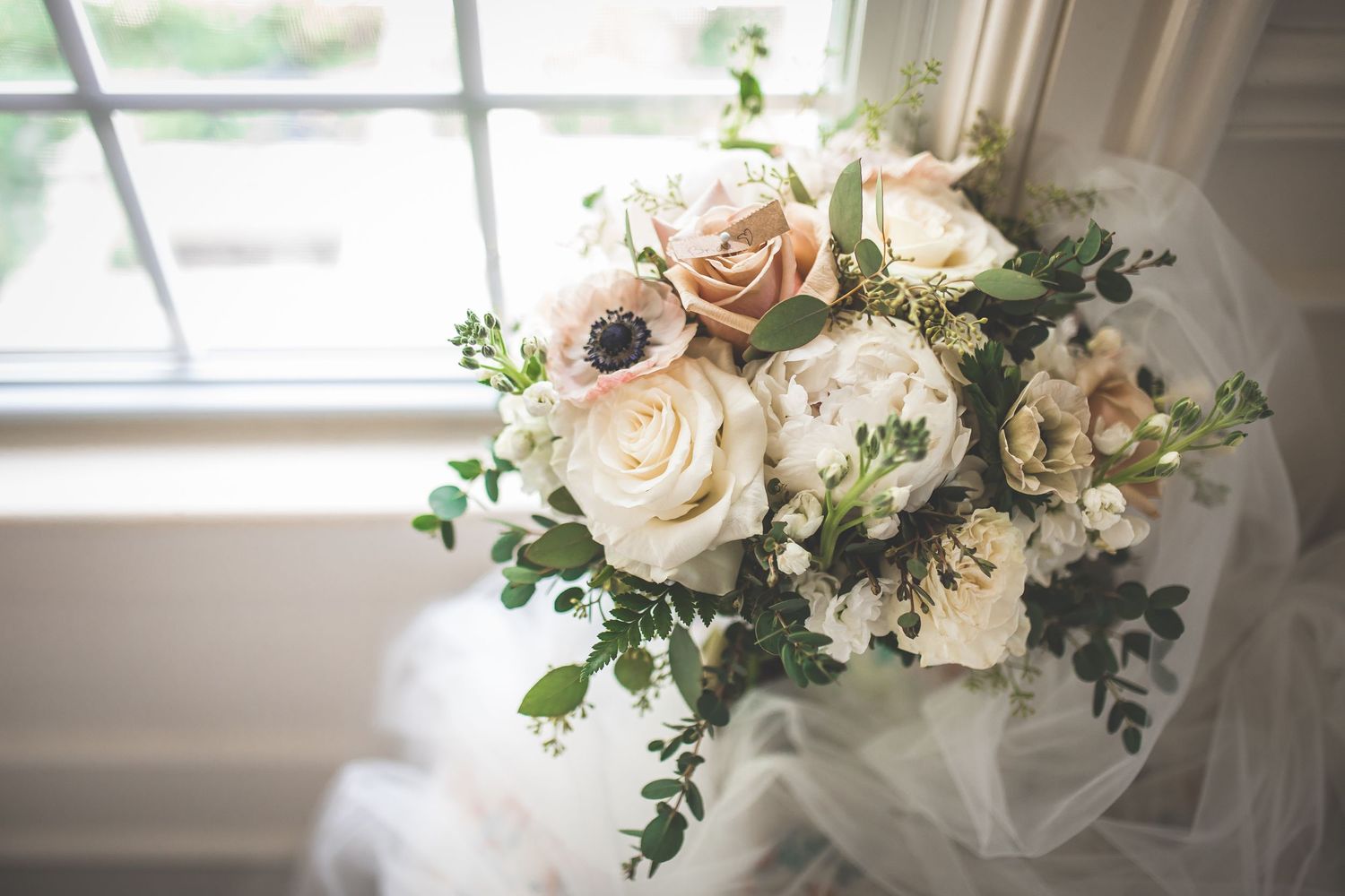 Elegant white and blush wedding bouquets arranged by a window with natural light.