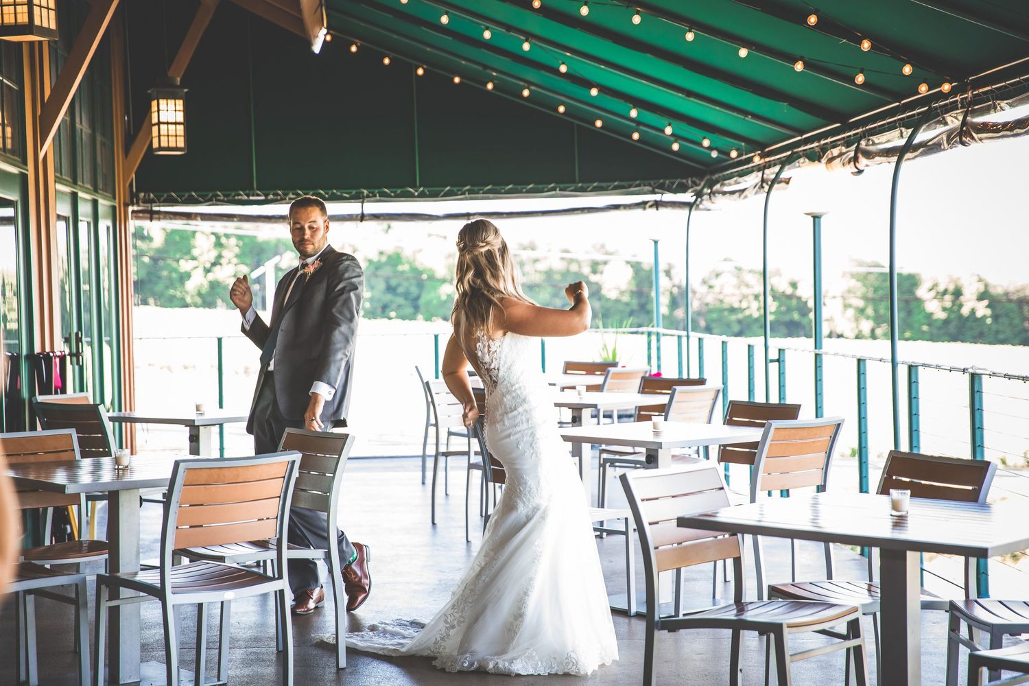 Newlyweds celebrating on covered outdoor patio with string lights overhead.