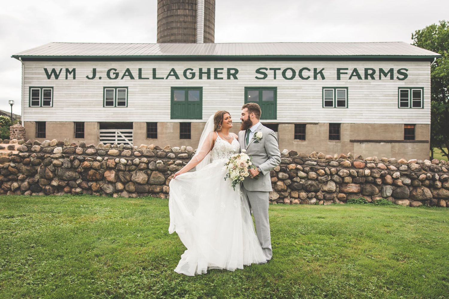 Wedding photos taken at Wm J Gallagher Stock Farms with stone wall and white buildings.