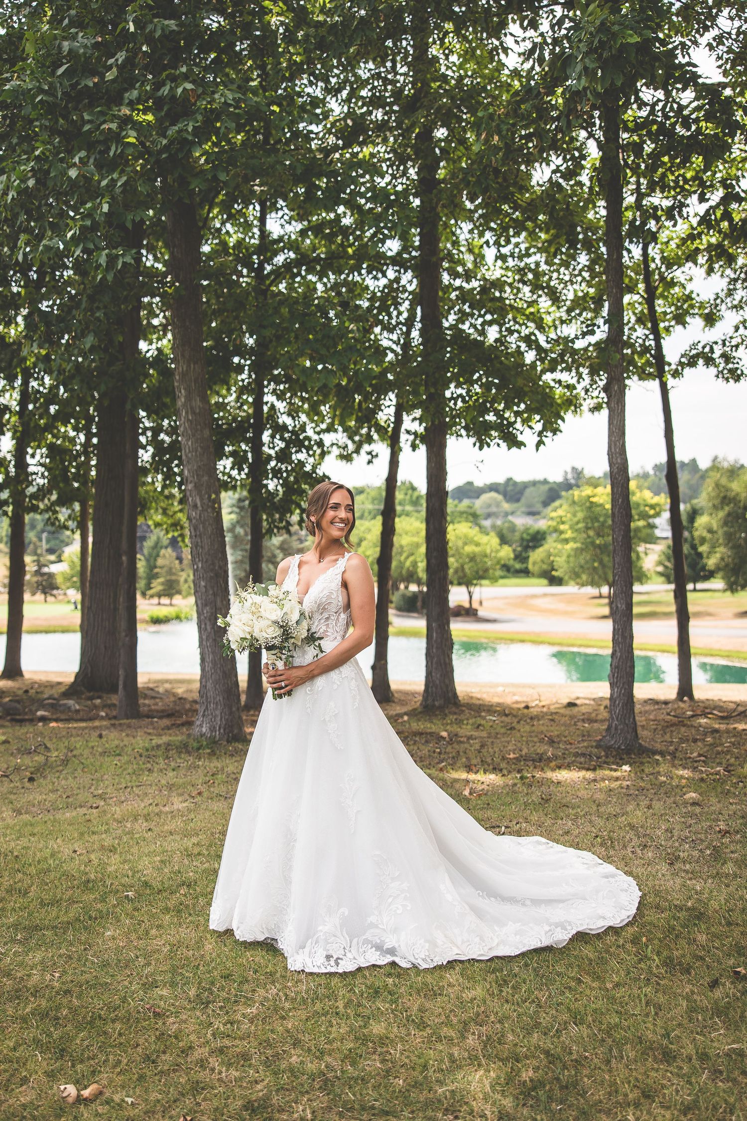 White wedding dress with lace details photographed outdoors among tall trees.