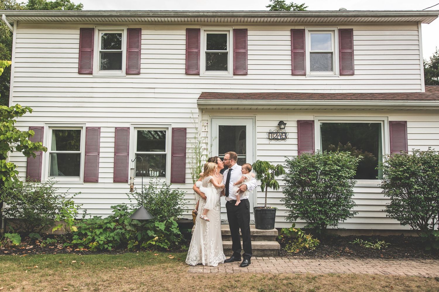Wedding party gathered outside a classic white colonial style house.