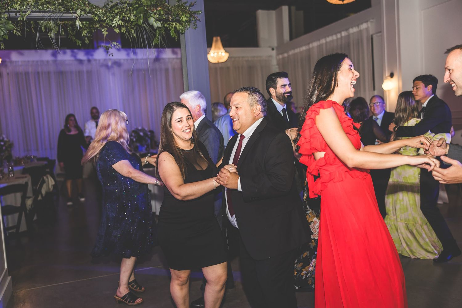 Guests dancing and celebrating at an evening wedding reception with colorful ambient lighting.