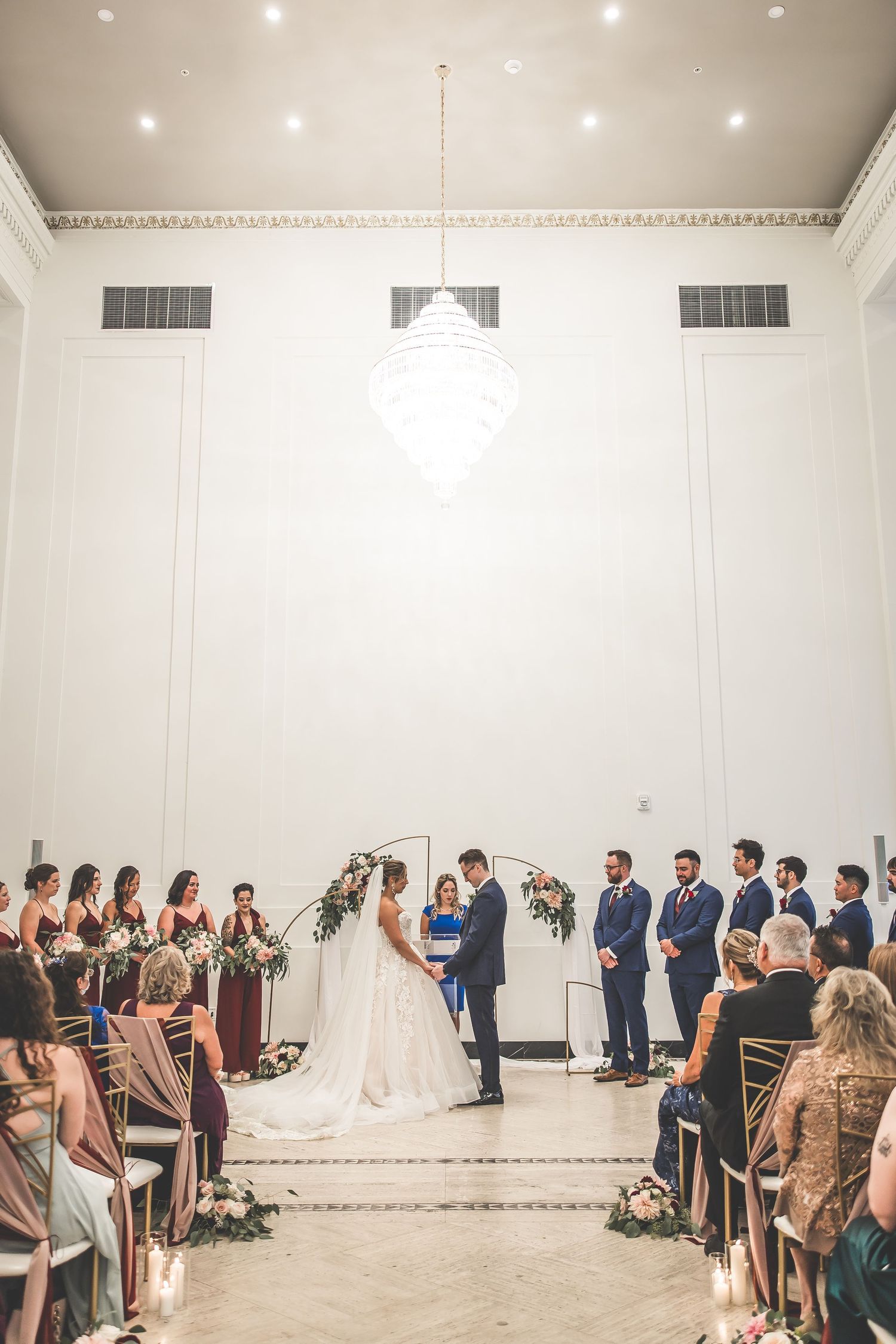 Wide angle view of wedding ceremony in progress in a bright white ballroom.