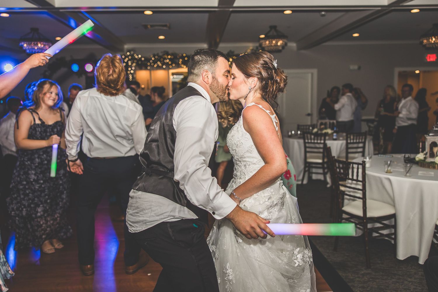 Guests dancing and celebrating at wedding reception with colorful lighting and glow sticks.