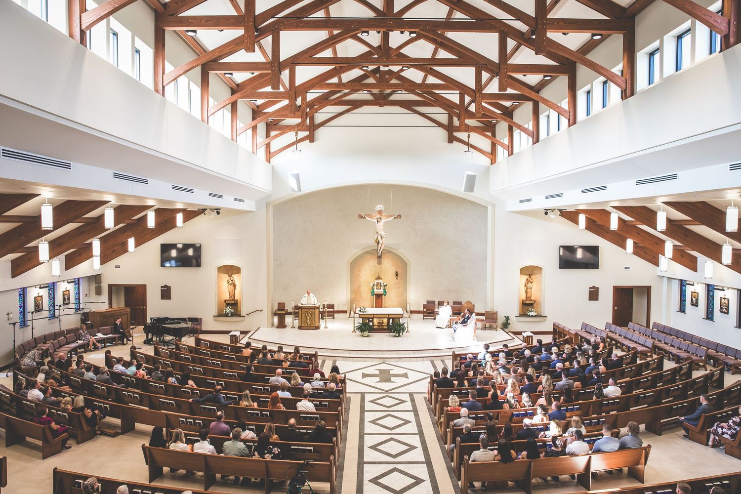 Panoramic view of a church filled with wedding guests under wooden beam architecture.