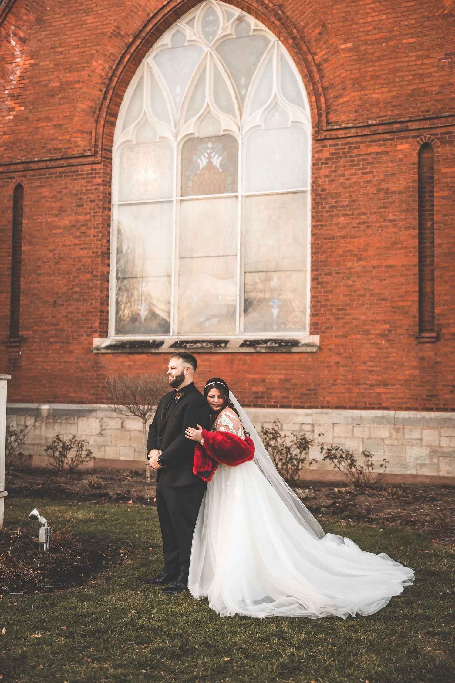 A romantic winter wedding photo shoot outside a historic red brick church with arched windows.