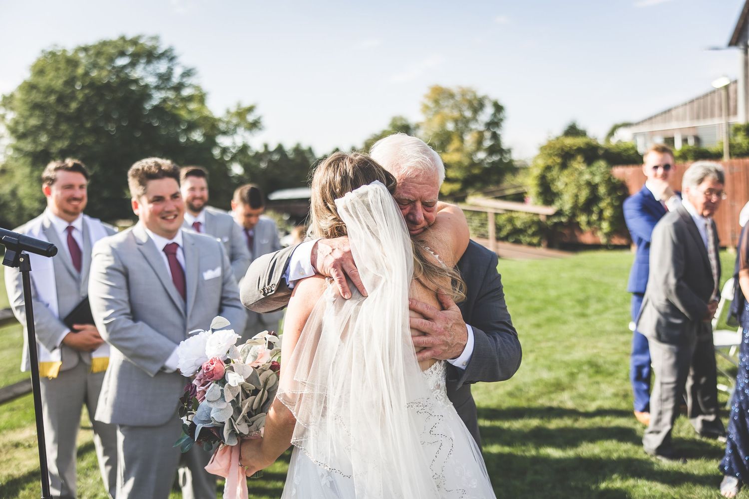Emotional outdoor wedding ceremony moment with guests watching in background.