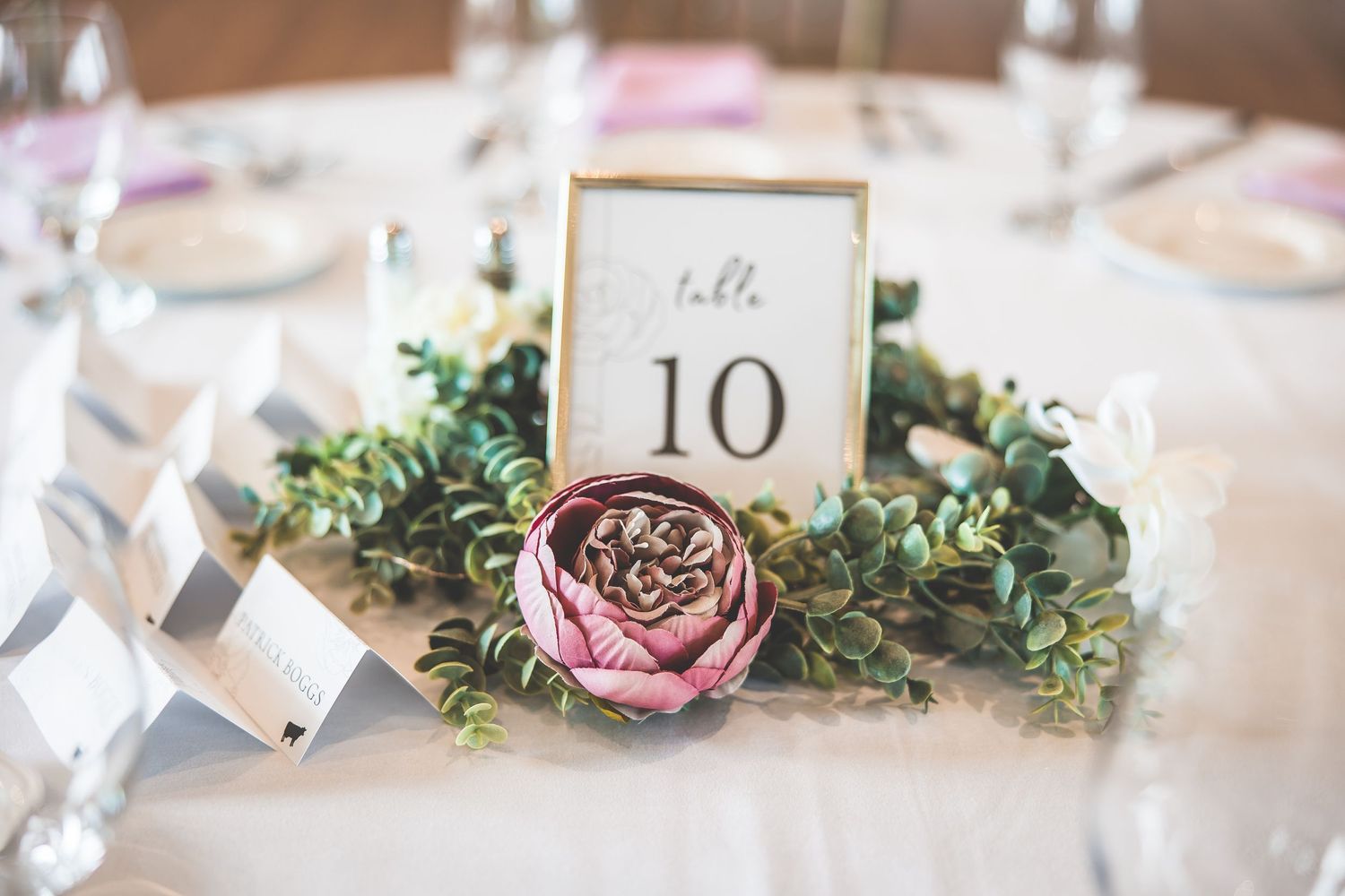 Wedding table number 10 displayed with pink rose and greenery centerpiece.