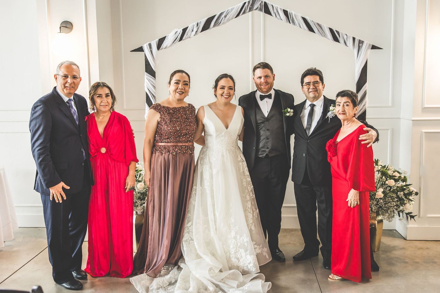 Wedding party members line up for photos wearing formal attire in red, burgundy and black.