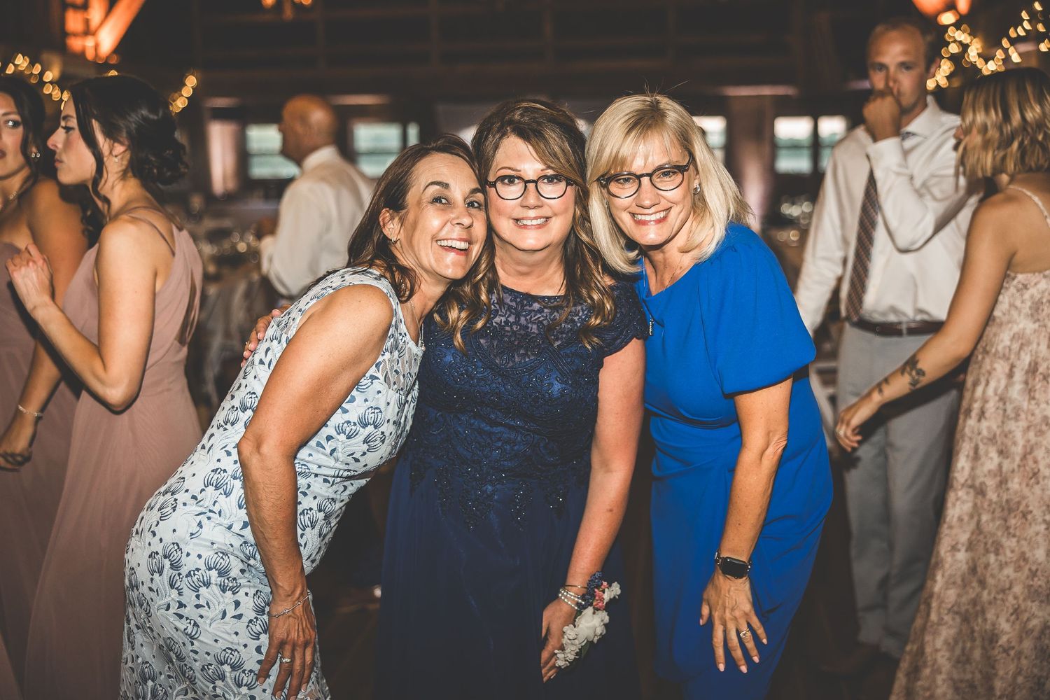 Wedding guests dancing and celebrating on a dance floor decorated with string lights at an evening reception.