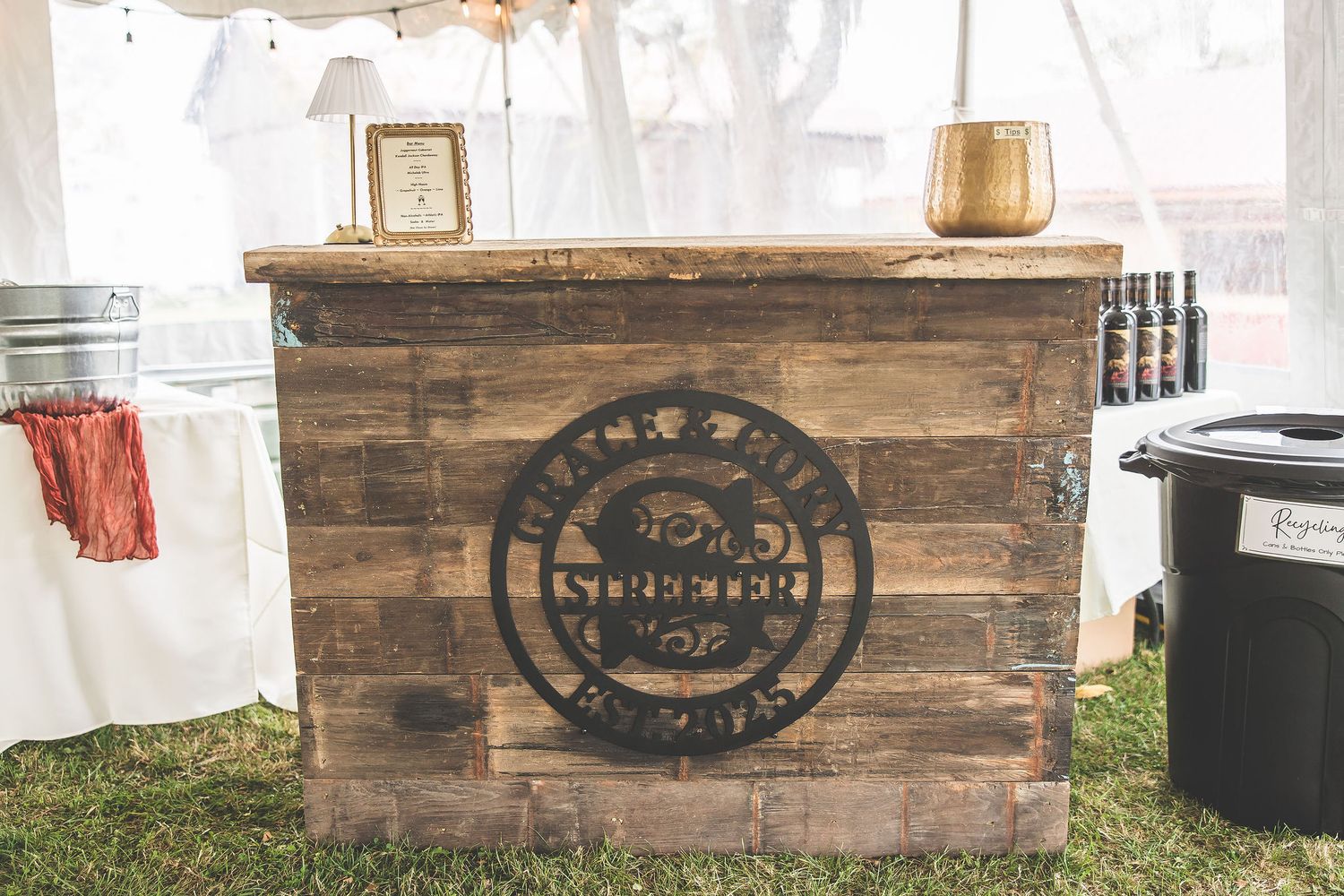 Rustic wooden bar setup with vintage signage at an outdoor wedding reception.