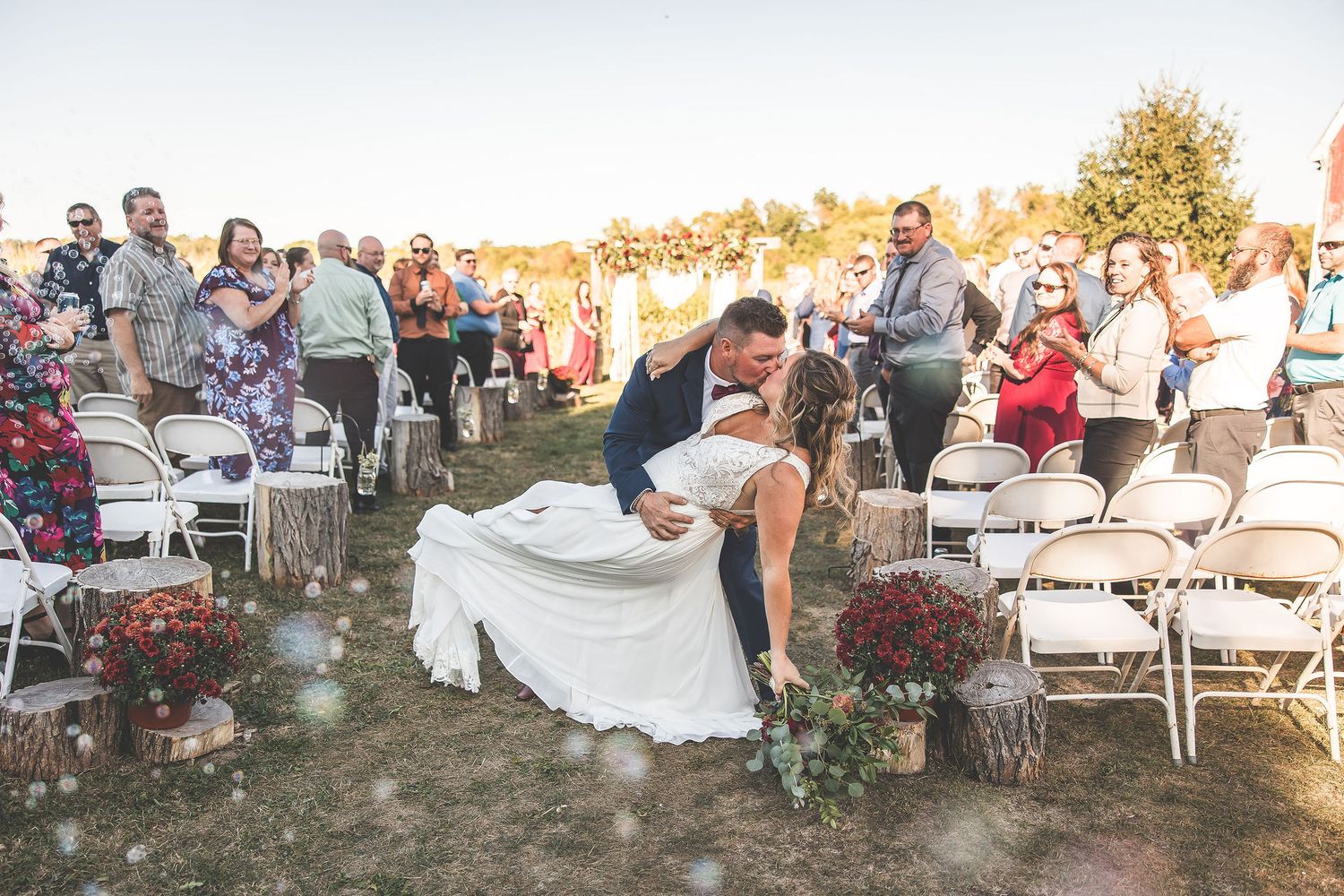 Wedding reception area with white tables and chairs set up on grass during golden hour.