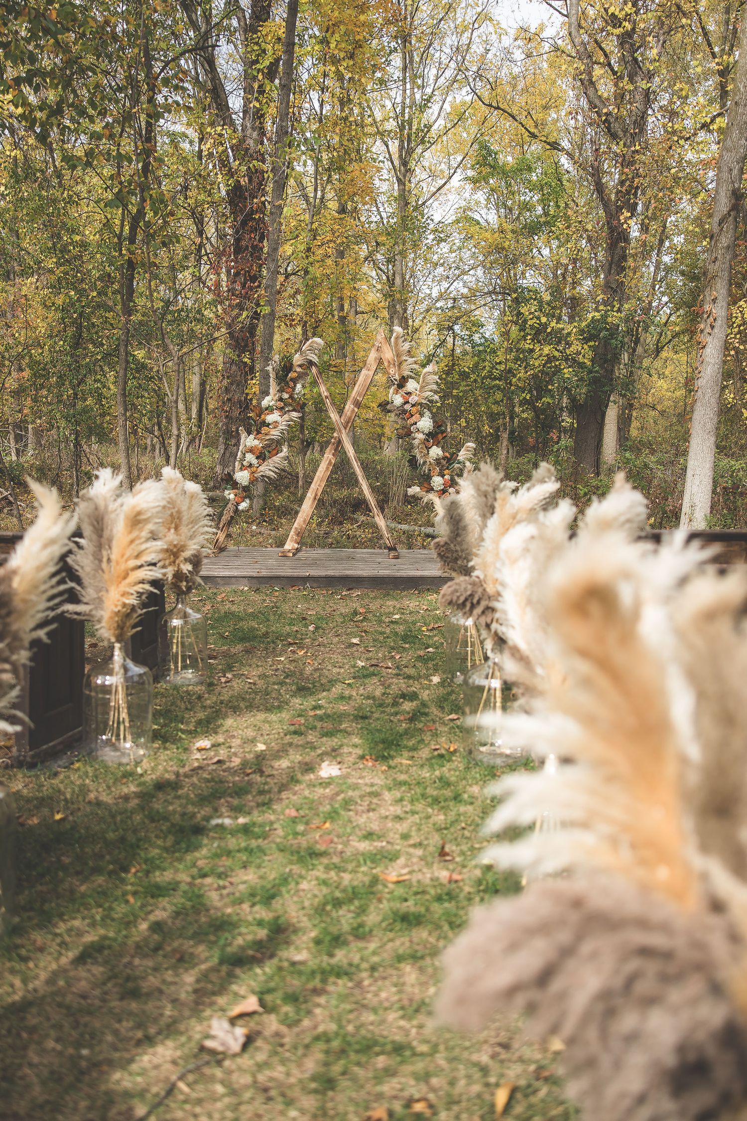 Rustic outdoor wedding venue with wooden benches surrounded by fall foliage.