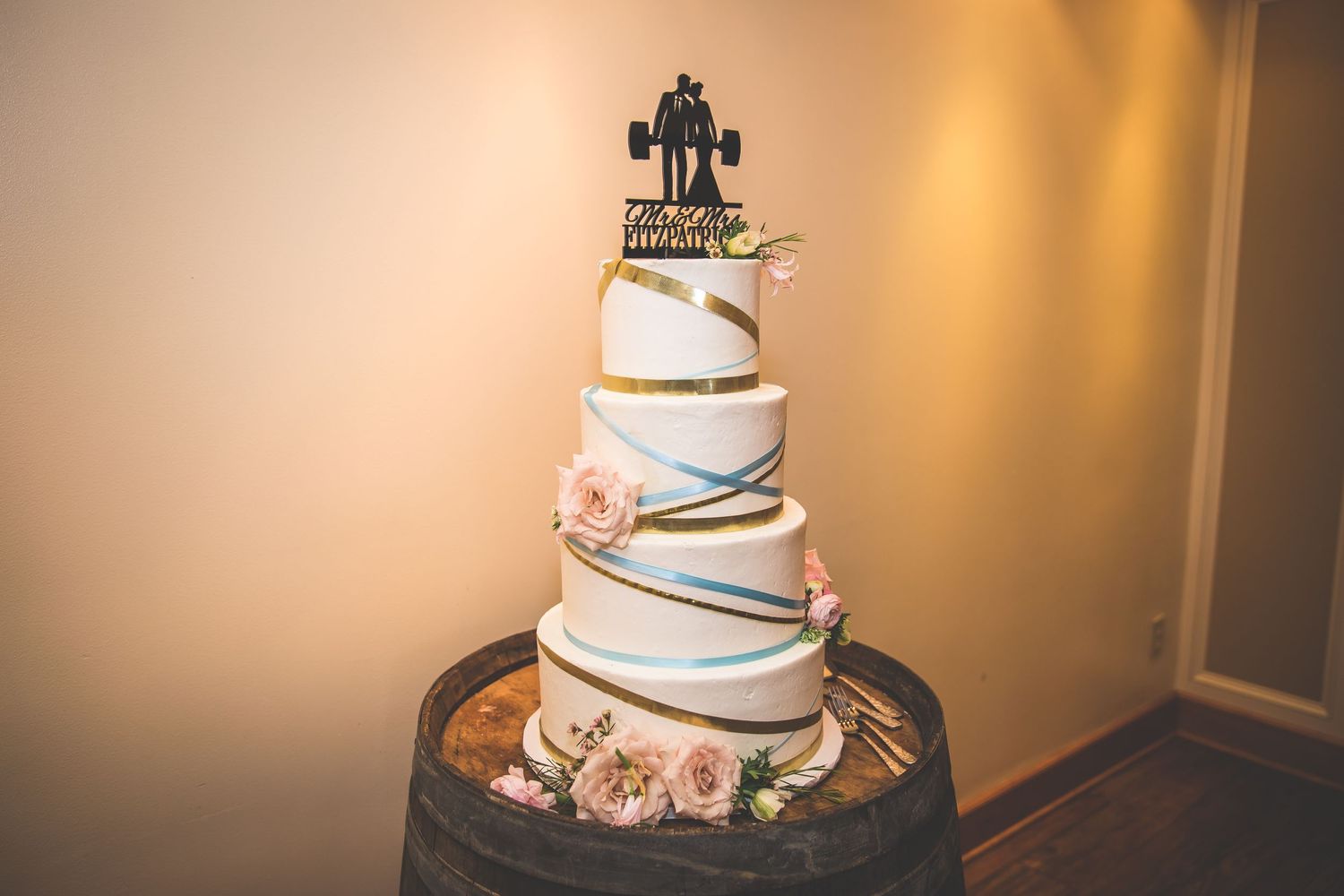 Elegant white wedding cake with blue ribbon trim displayed in warm indoor lighting.